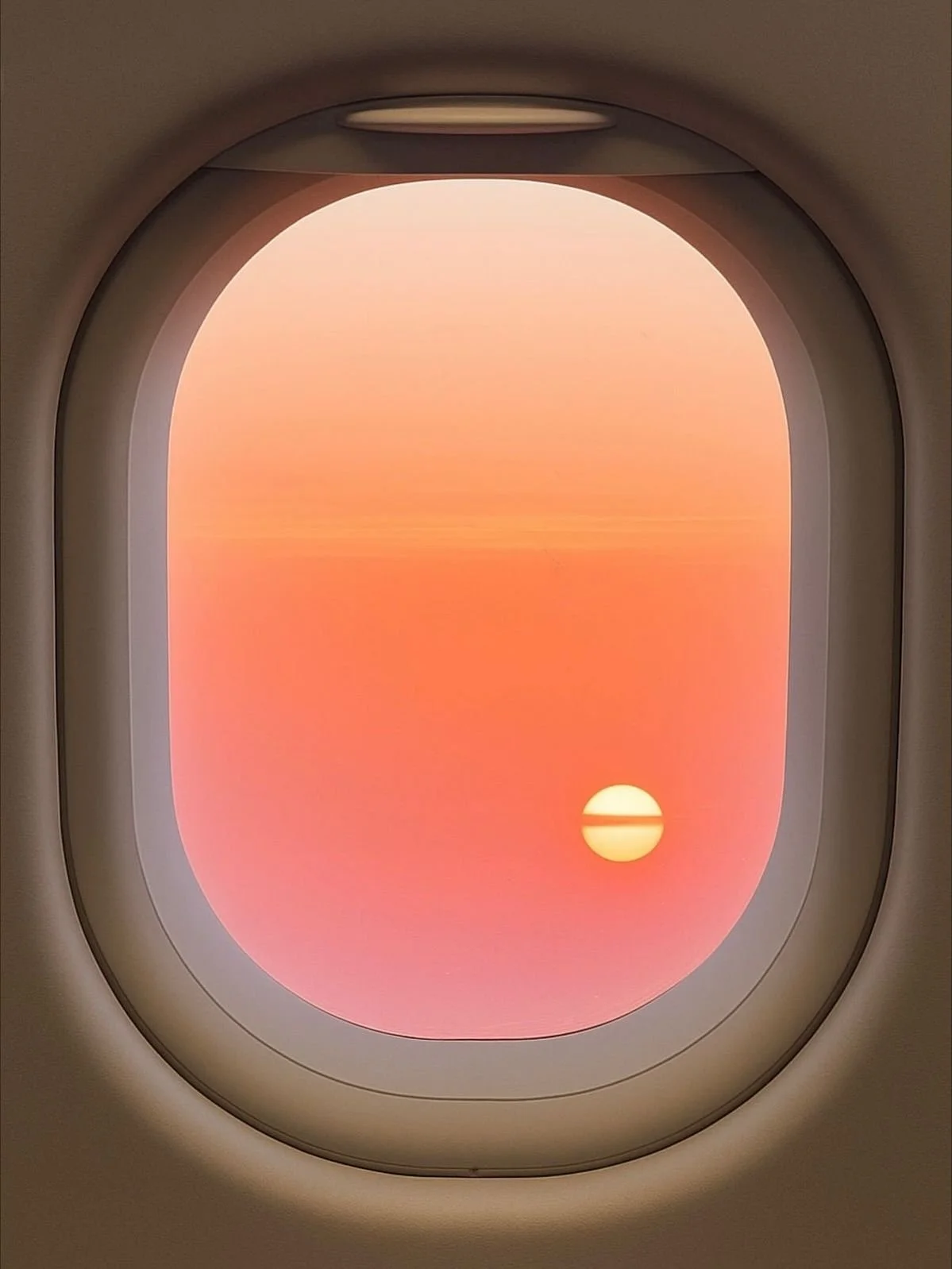 View through an airplane window showing a sunset with a glowing sun and a colorful sky in shades of orange and pink.
