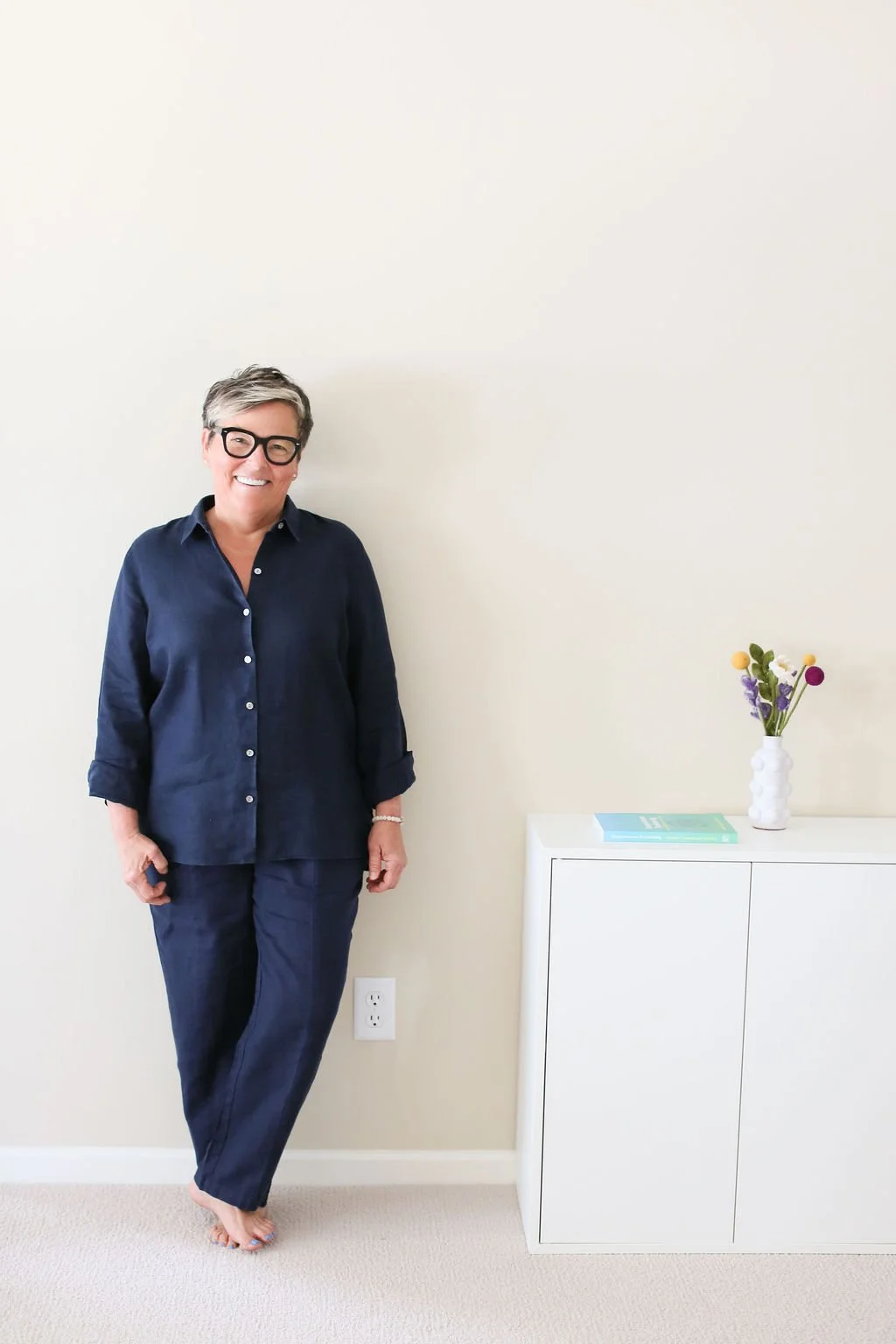 Home coach standing in a calm room beside the Compassionate Decluttering book, representing support for women who feel overwhelmed at home.