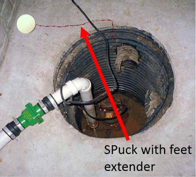 A sump with feet extender inside a basement floor drain, with a green pipe fitting and electrical wiring connected to it.
