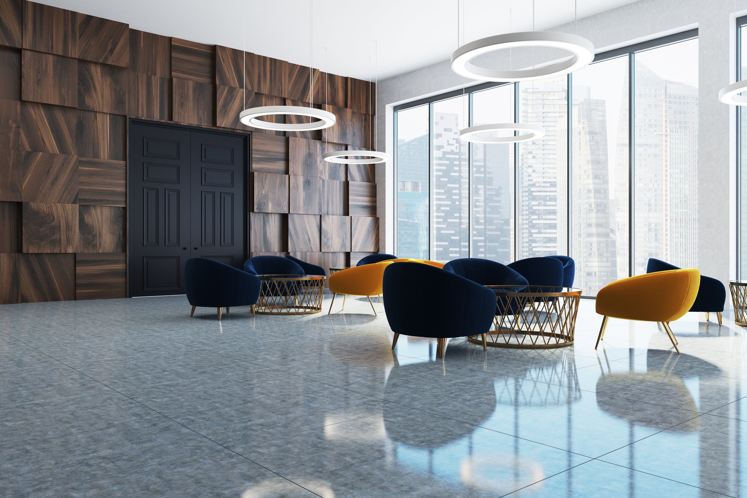 Modern interior space with large glass windows, wooden wall accents, circular white pendant lights, and colorful seating including blue and yellow chairs on a shiny tiled floor.