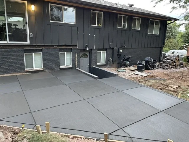 Newly poured concrete driveway with expansion joints in front of a dark gray house with large windows.