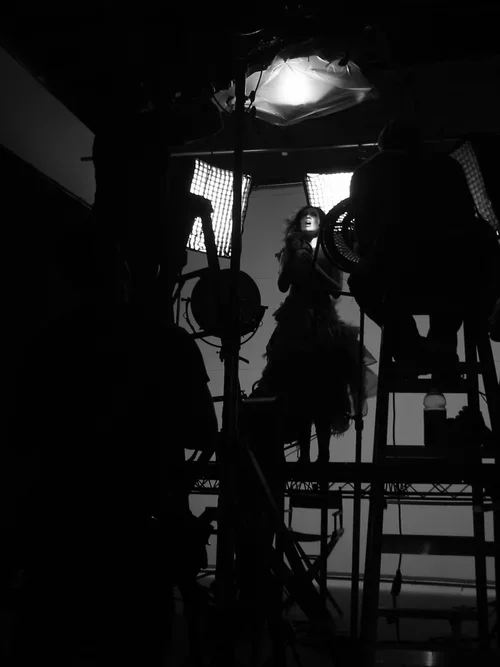 A woman posing for a photoshoot with studio lighting and equipment in a black-and-white setting.