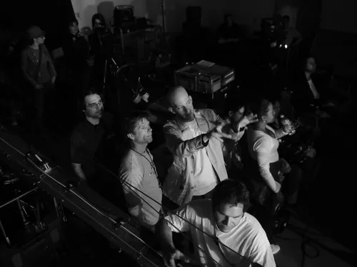 A black and white photo of a group of people at a live music event, some playing musical instruments and others watching.