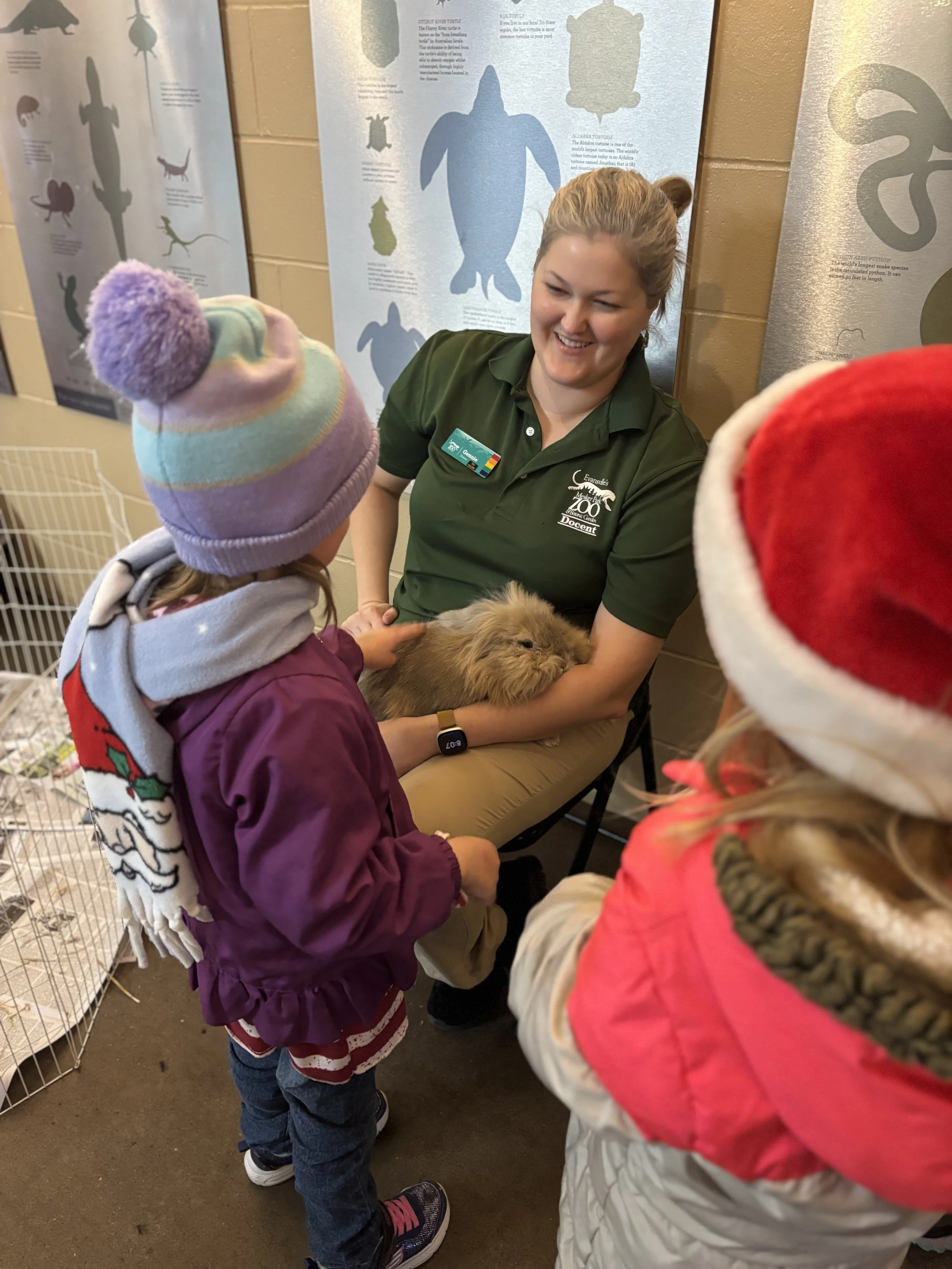 A zoo volunteer in a green shirt, holding our ambassador rabbit for guest interactions.