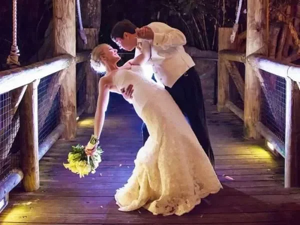 A bride and groom dancing closely on a wooden bridge during their wedding reception at night.