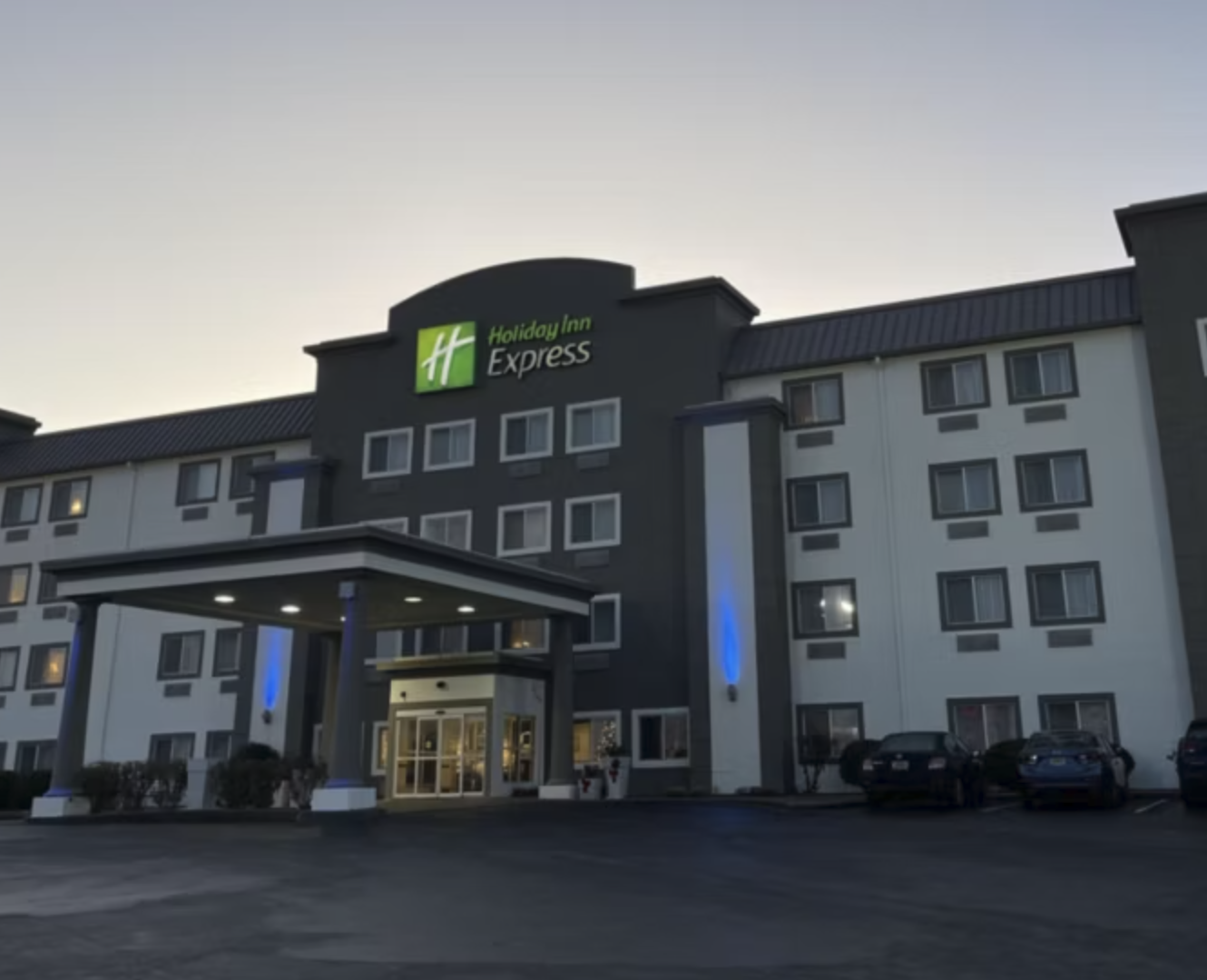 Exterior of a Holiday Inn Express hotel with a lit entrance and parking lot at dusk