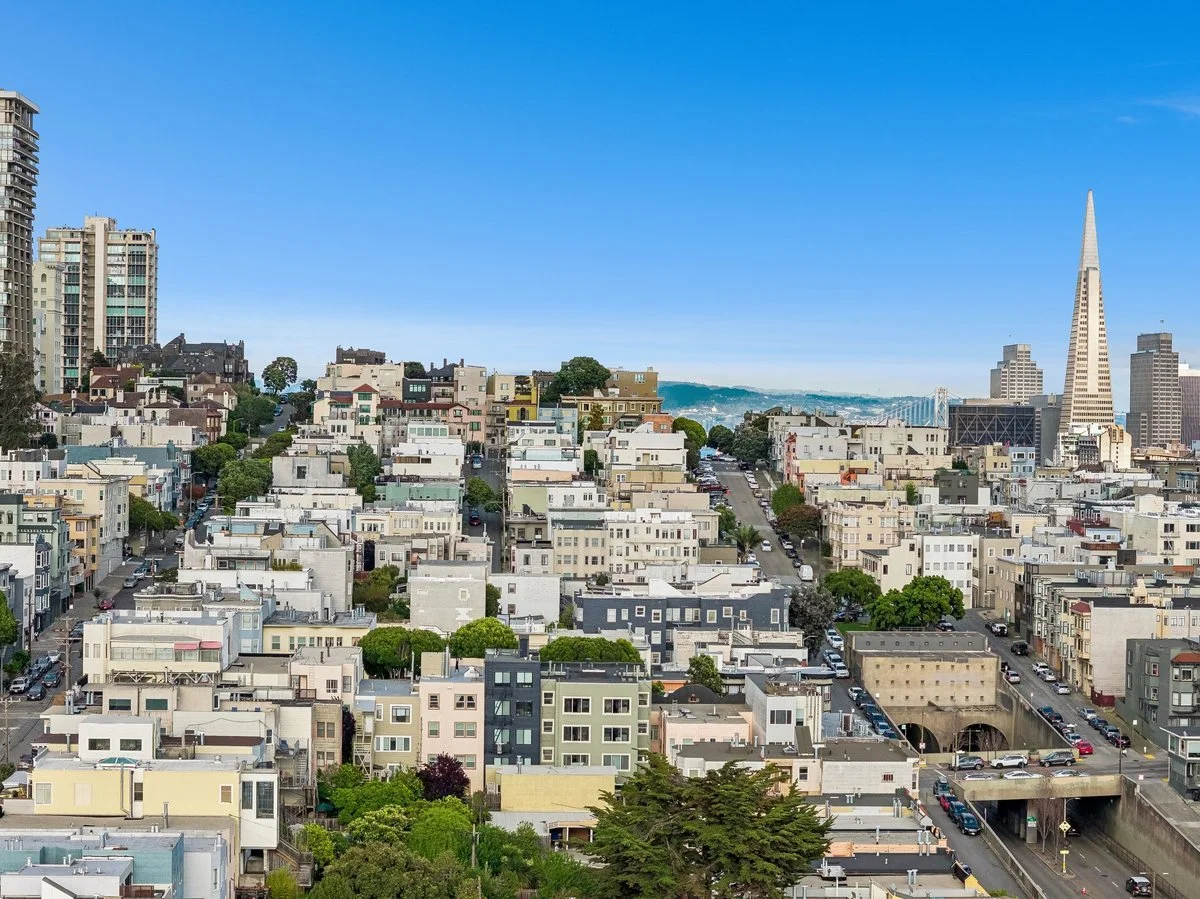 Cityscape of San Francisco with buildings, streets, and the Transamerica Pyramid skyscraper in the background under a blue sky.