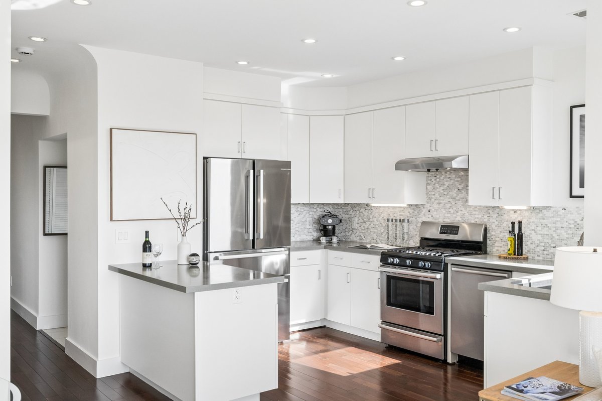 Modern kitchen with white cabinets, stainless steel appliances, and a mosaic tile backsplash.