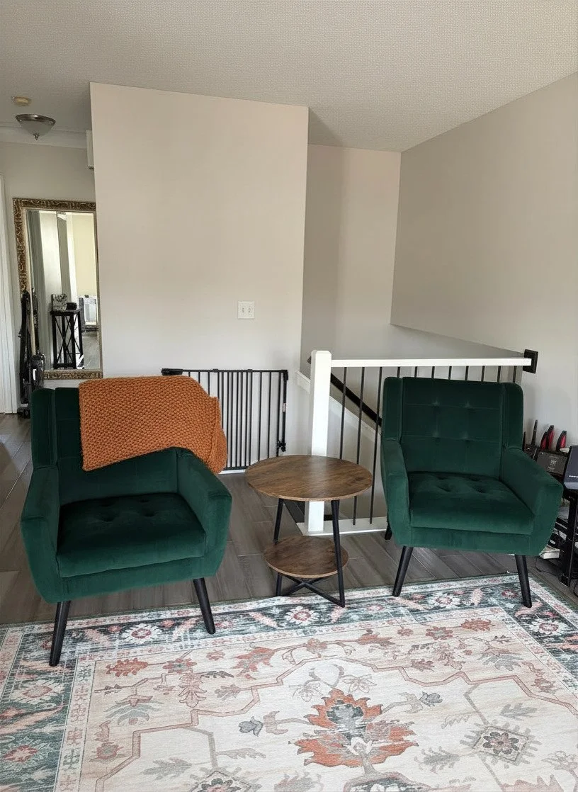 Living room corner with two green armchairs, a wooden side table, and a patterned area rug.