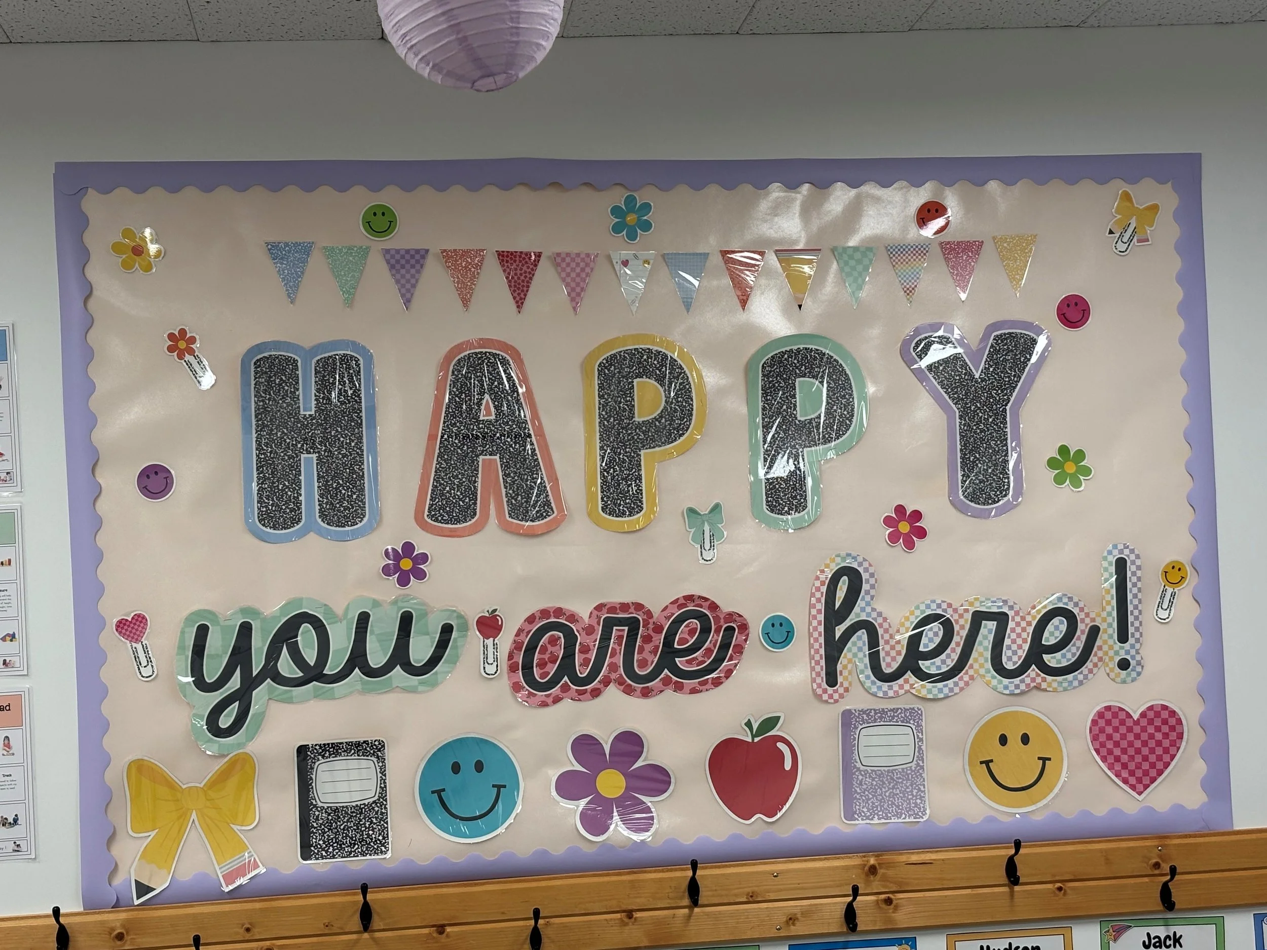 Colorful classroom bulletin board with the words 'HAPPY' prominently displayed, decorated with smiley faces, flowers, butterflies, and bunting flags.