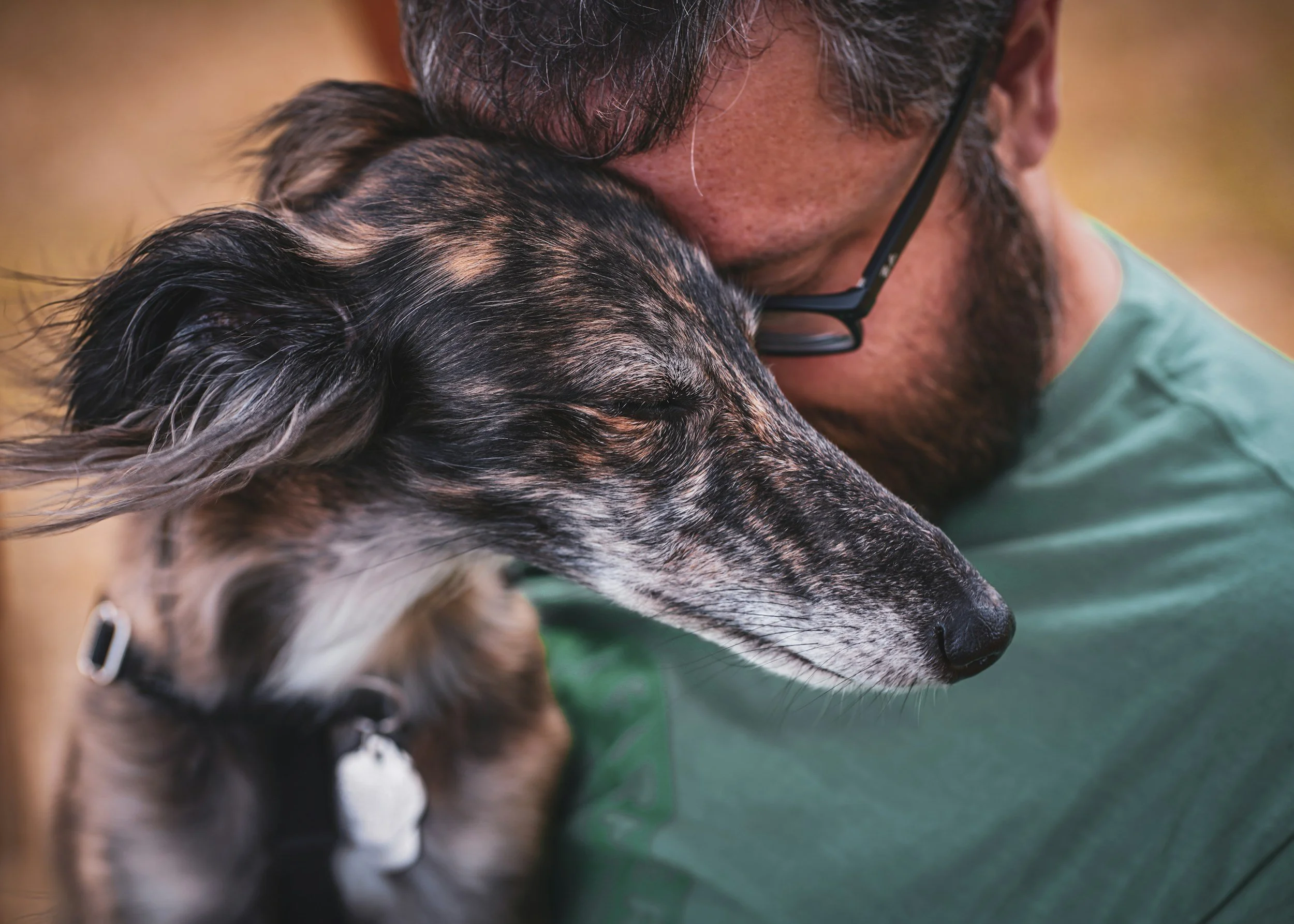 A man hugging and cuddling his dog outdoors, both with eyes closed, showing affection and bond