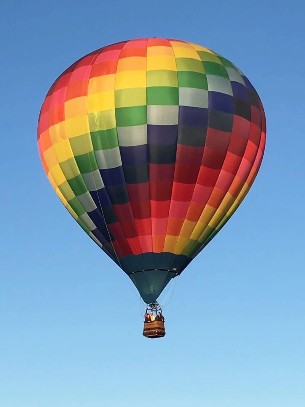 Colorful rainbow checkered hot air balloon floating in clear blue sky.