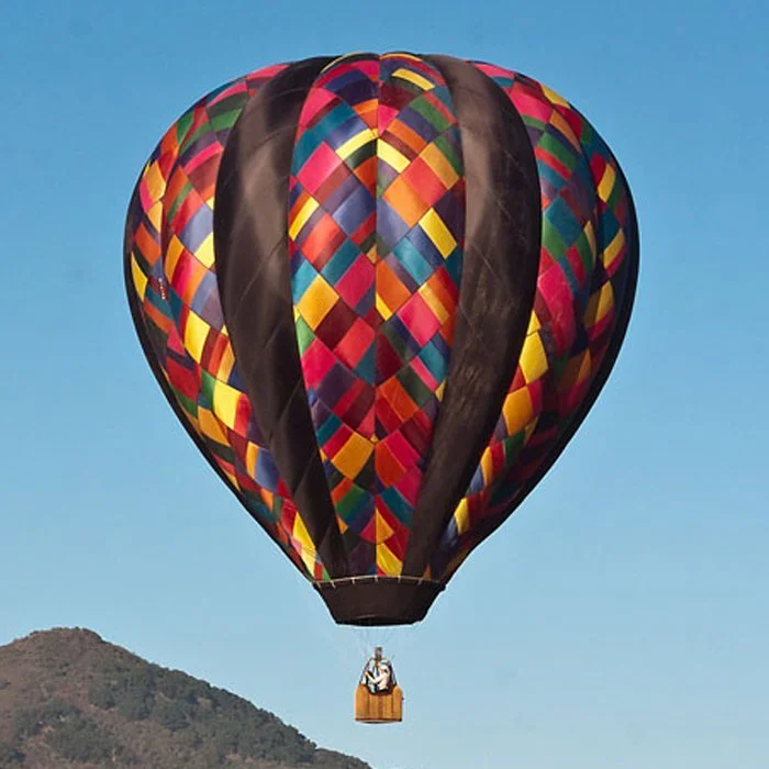 Colorful hot air balloon in the sky with a patterned design, floating over a mountain landscape.