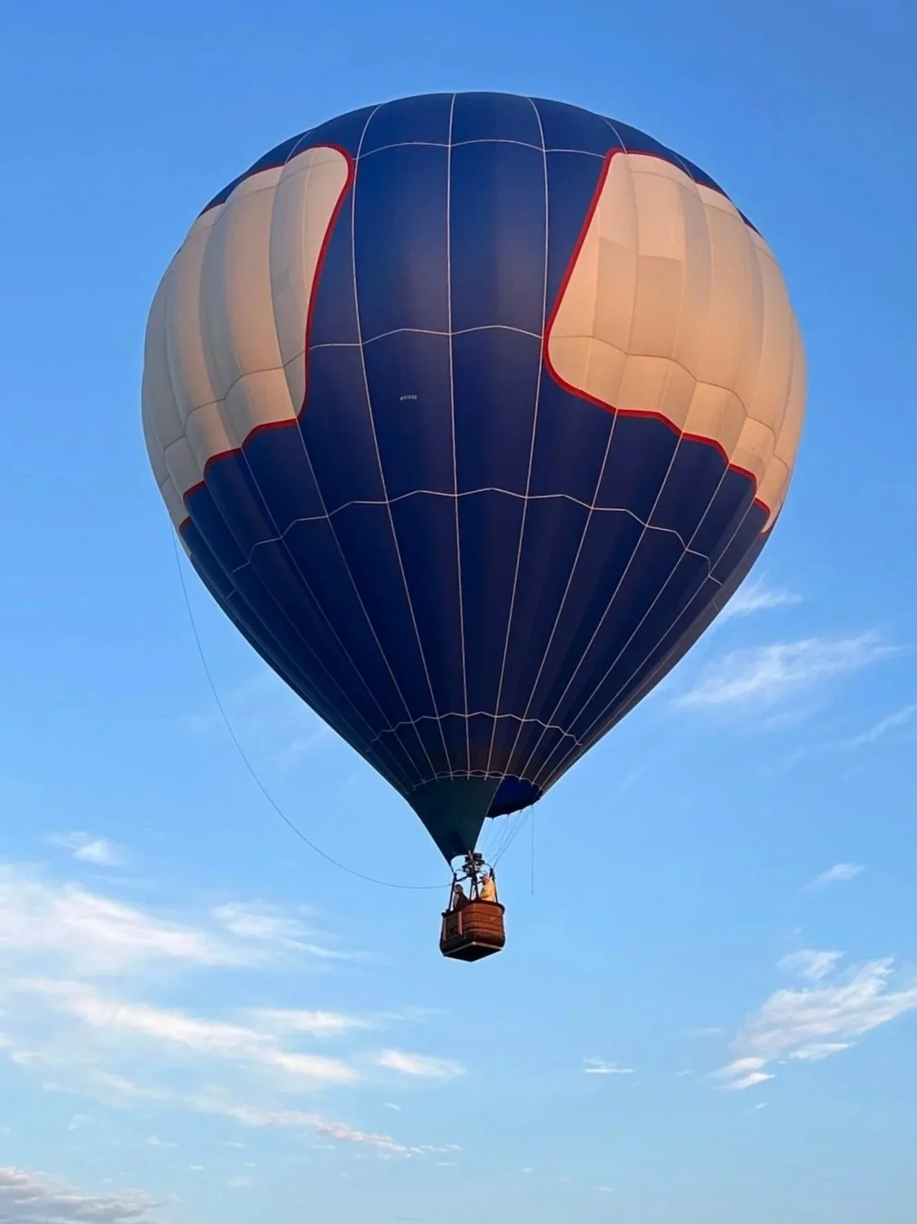 A hot air balloon with a dark blue and beige design floating in a clear blue sky.