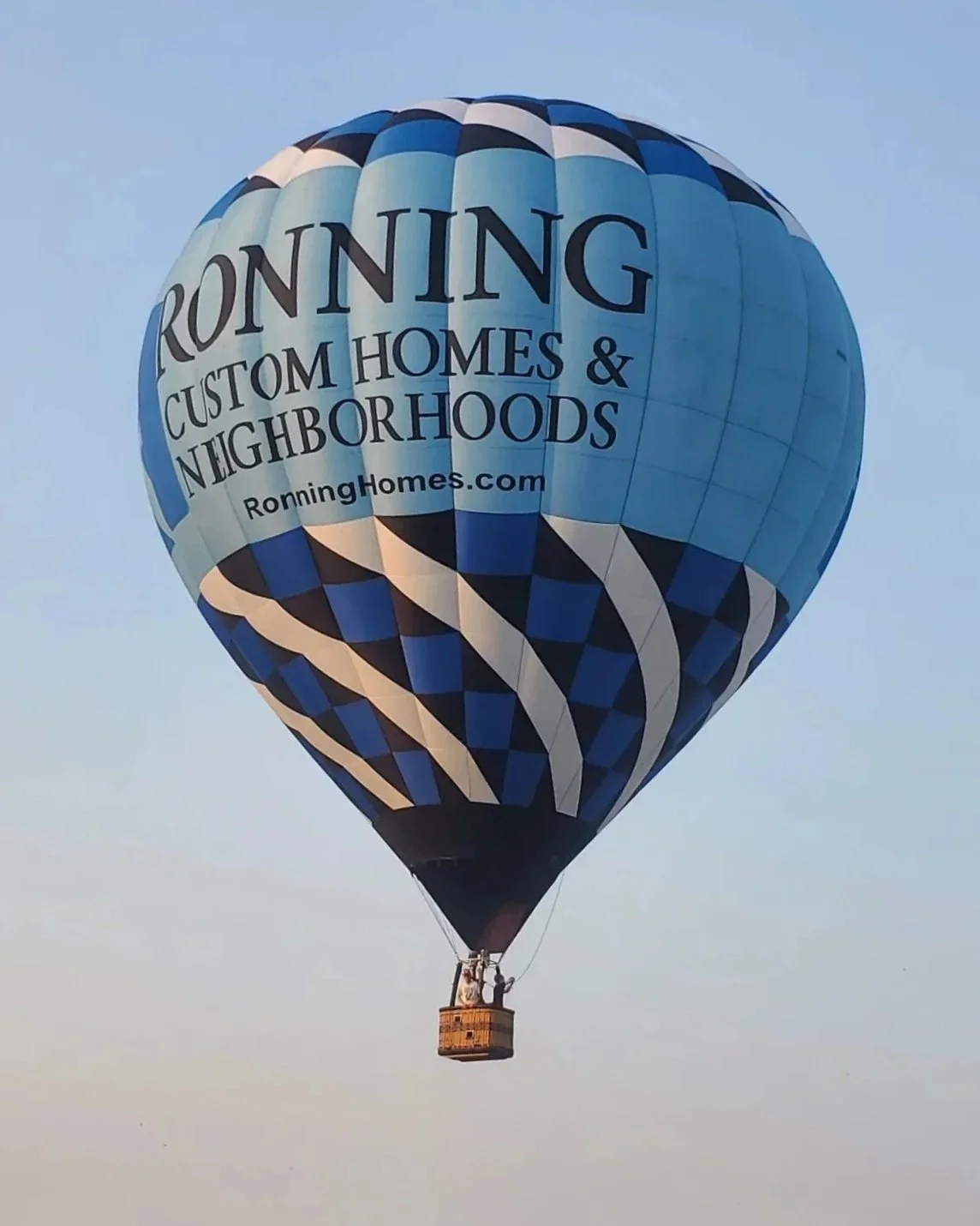 Hot air balloon with blue and black pattern, advertising Ronning Custom Homes & Neighborhoods, flying in the sky.