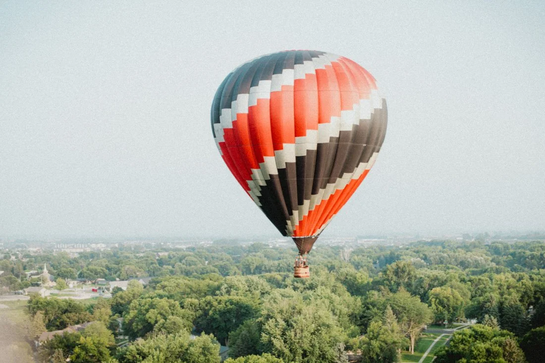 Colorful hot air balloon flying above a lush green landscape.
