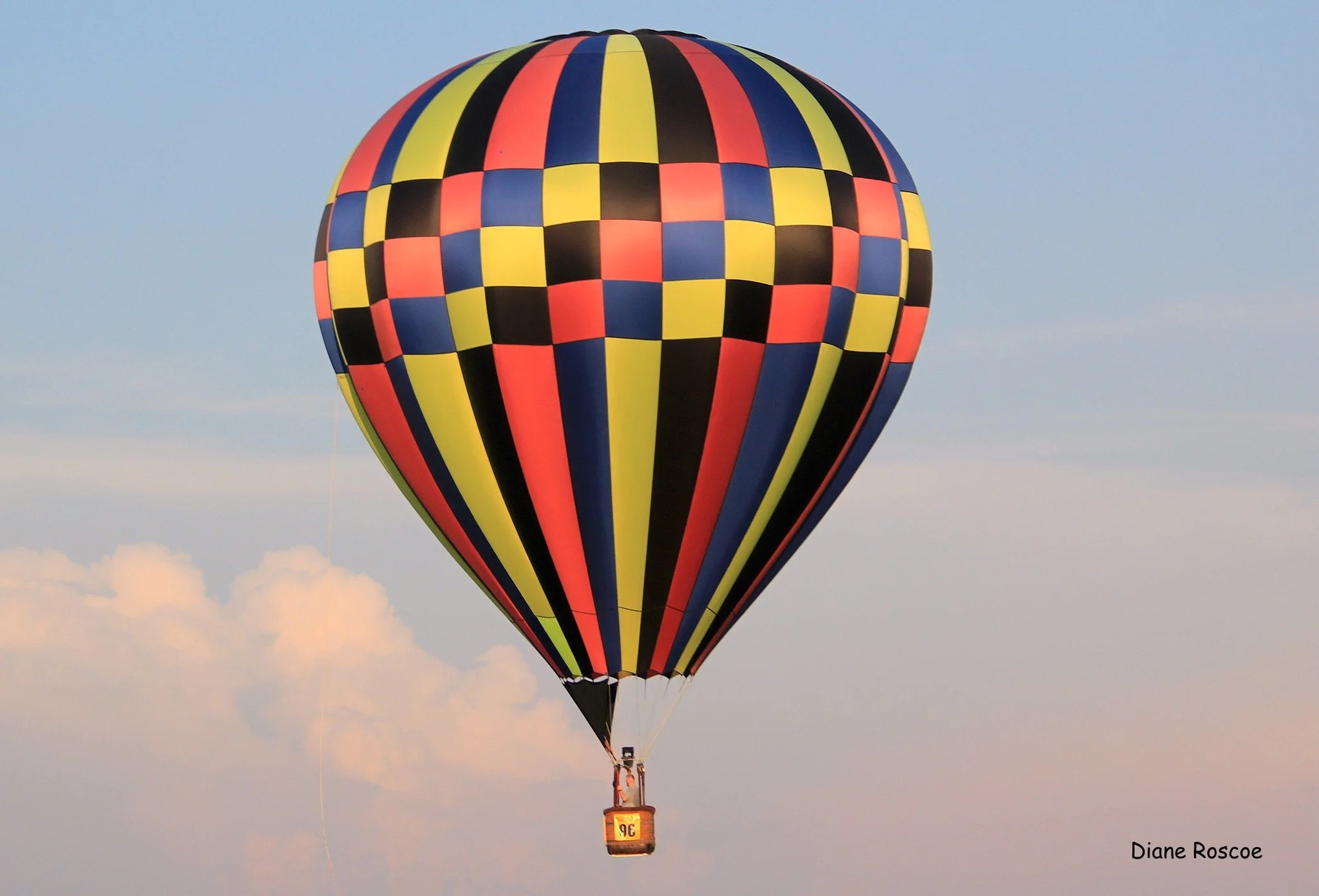 Colorful hot air balloon with a checkered pattern in yellow, blue, red, and black floating in the sky during daytime.