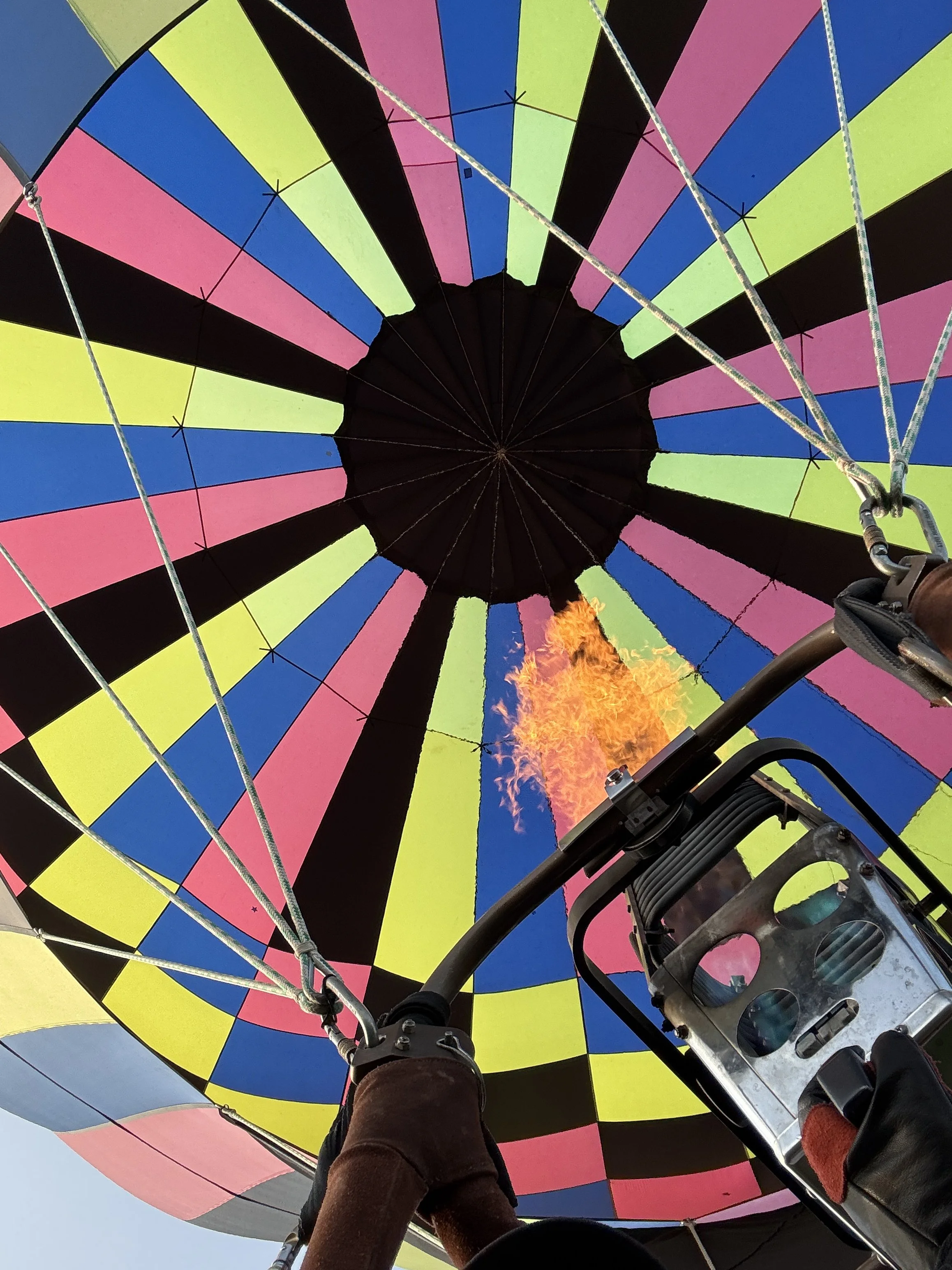 Looking up inside a hot air balloon with colorful vertical stripes of pink, yellow, blue, and black, as the flame heats the air.