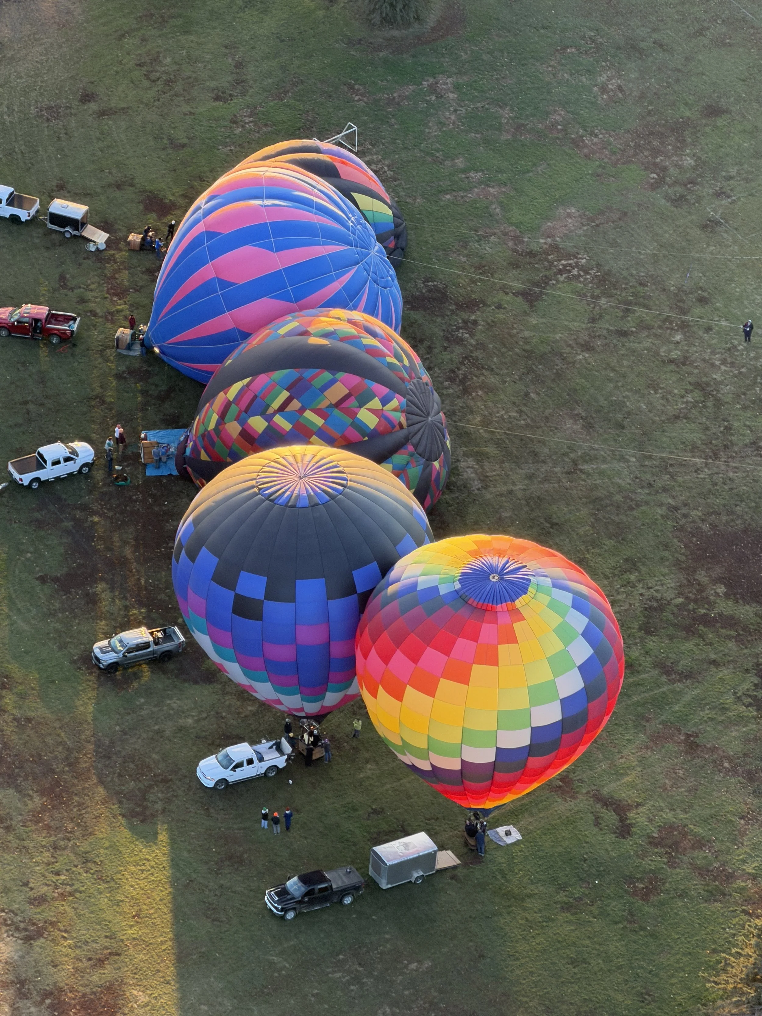 Multiple colorful hot air balloons on the ground with vehicles and people preparing for flight.