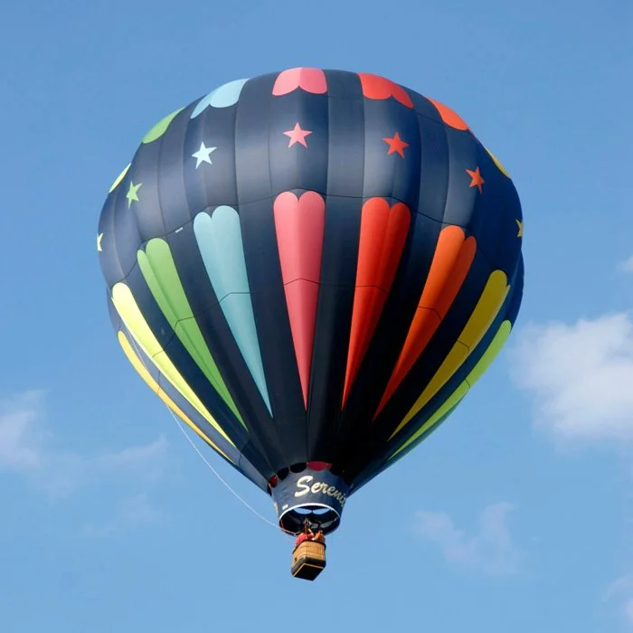 Colorful hot air balloon with star and stripe patterns flying in a clear blue sky.