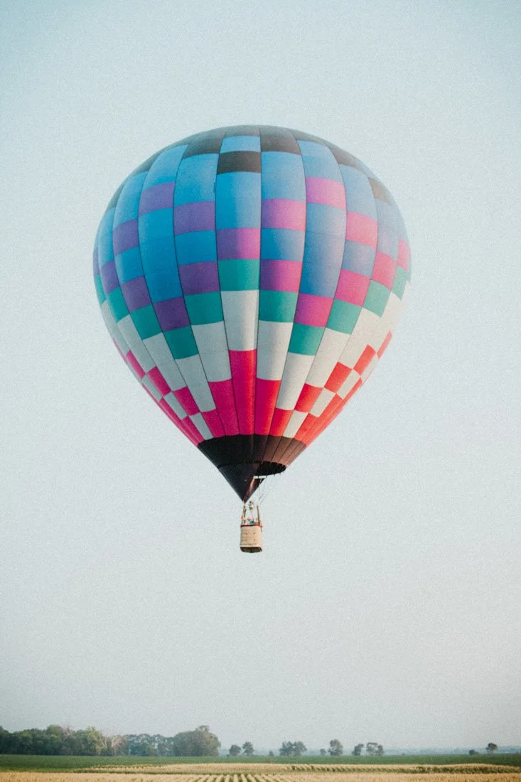 Colorful hot air balloon flying in the sky above a flat landscape with sparse trees.