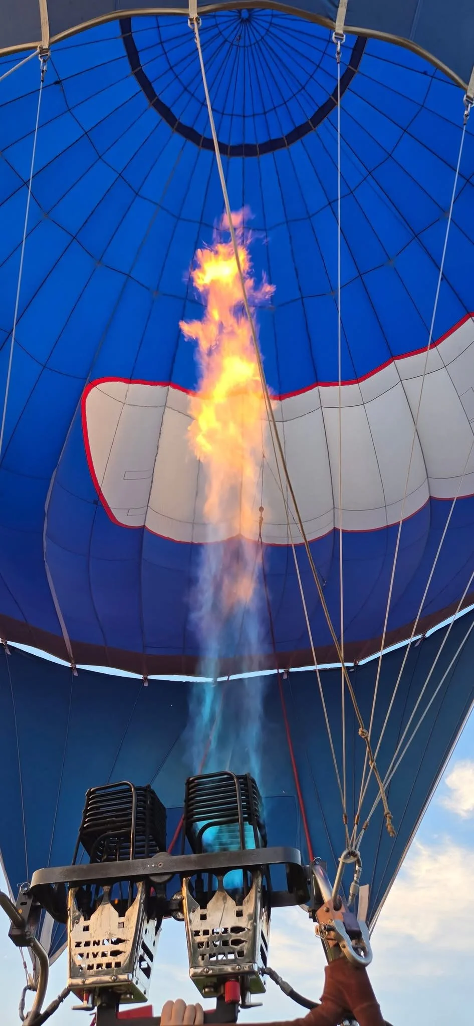 Hot air balloon with a blue and white envelope, with flames from the burner heating the air inside.