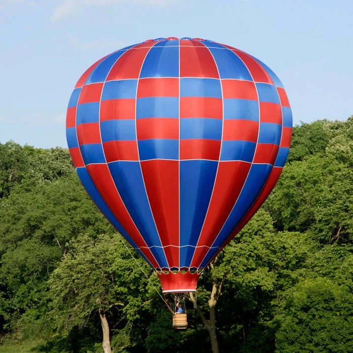 Colorful hot air balloon with red and blue checkered pattern floating above green trees.