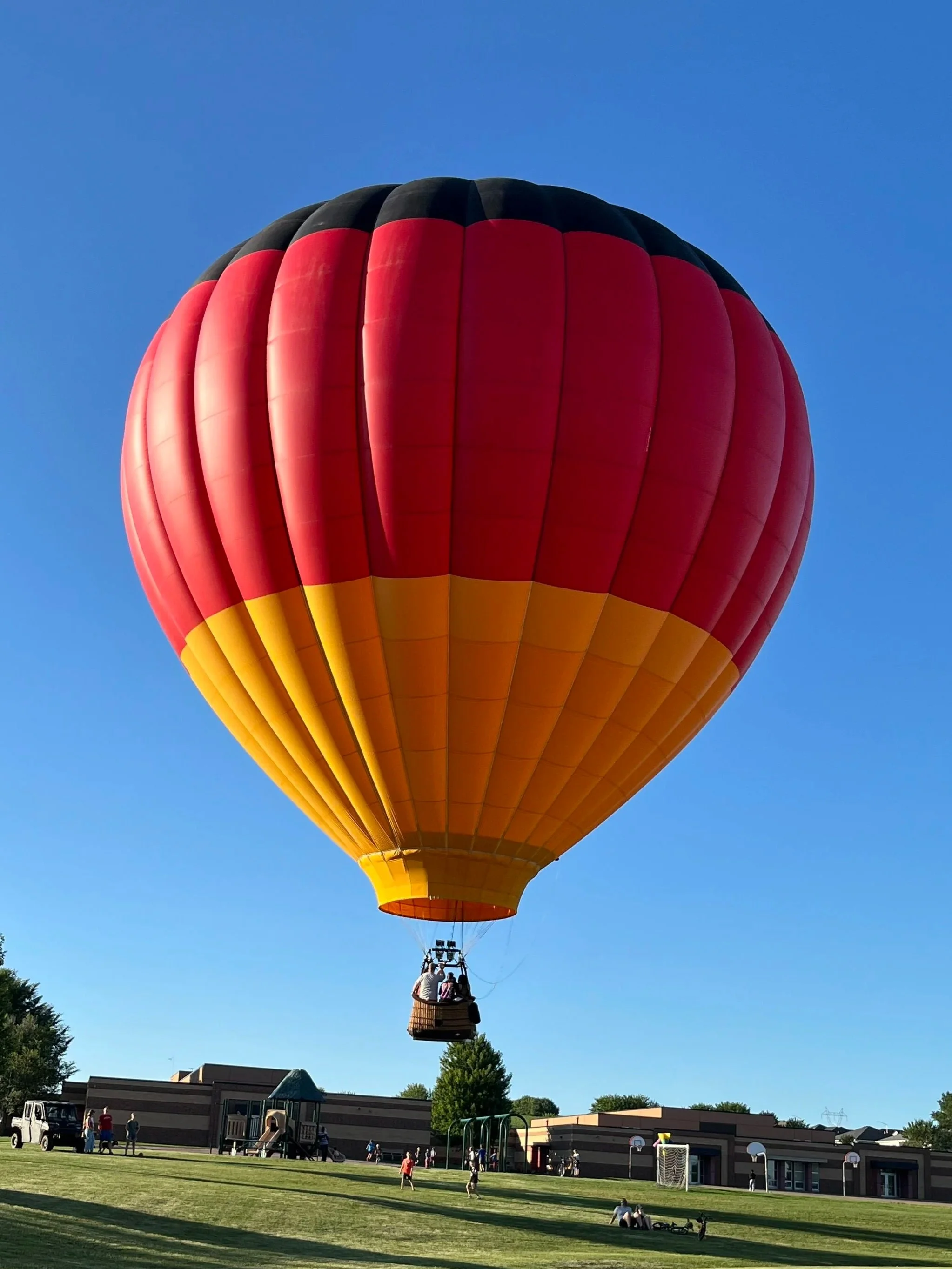Colorful hot air balloon floating above a park on a clear day.