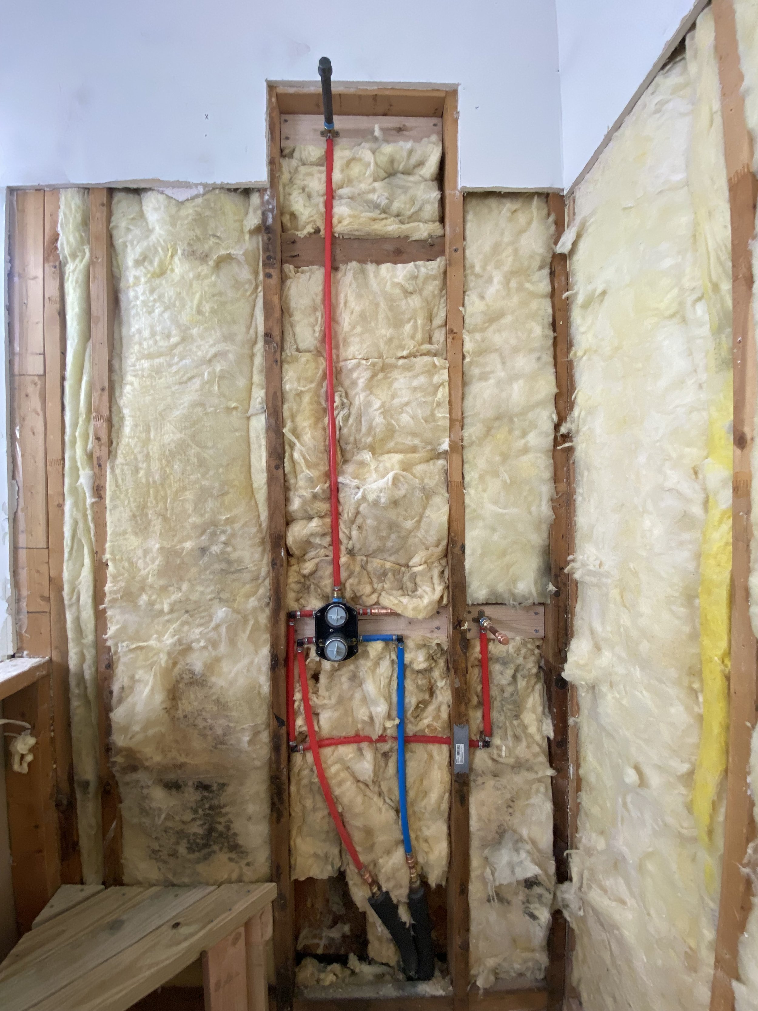 Interior of a wall with insulation and plumbing pipes installed for a renovation project.