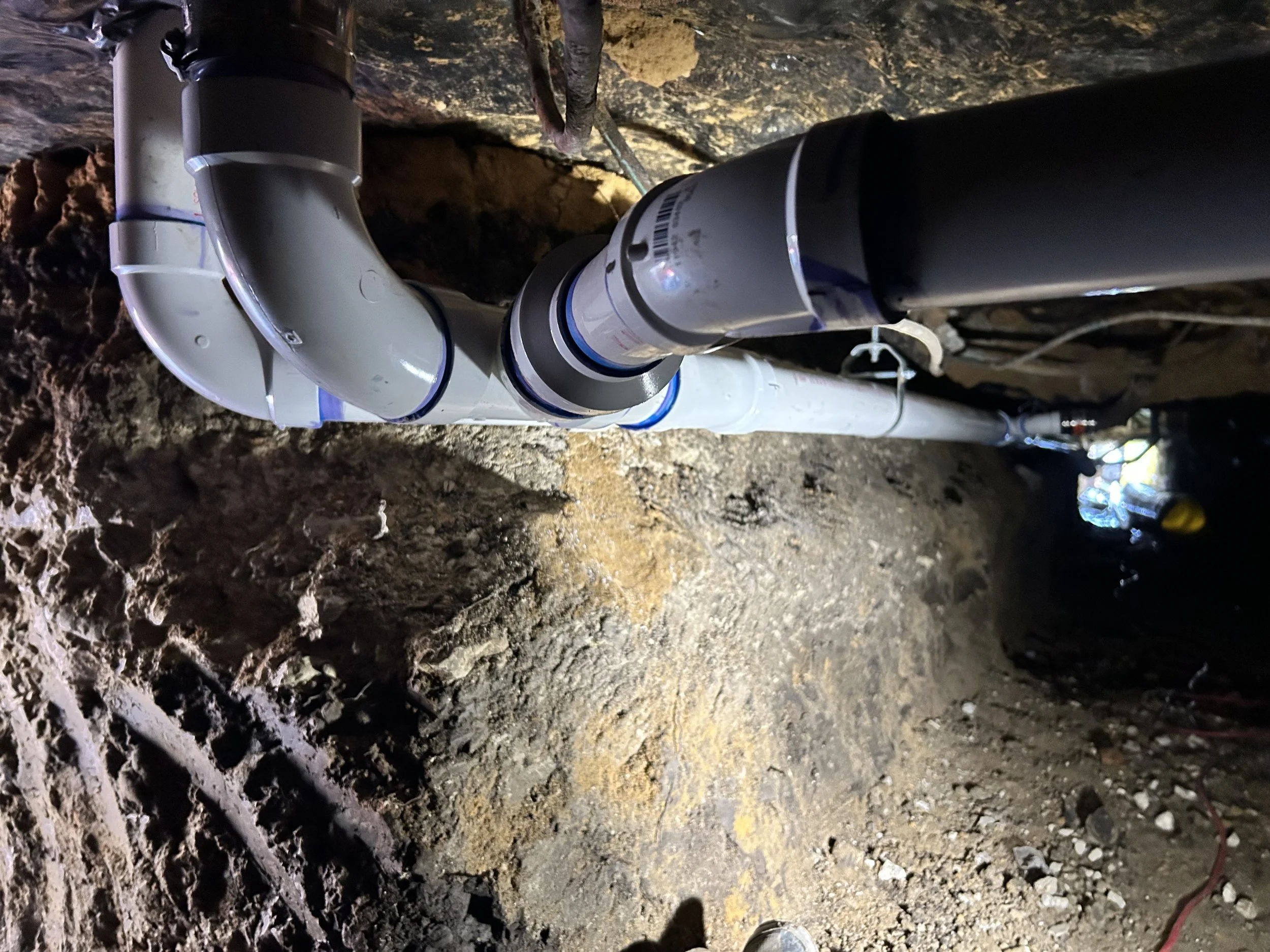 Underground plumbing pipes installed in a construction site or tunnel, with visible dirt and rock walls.