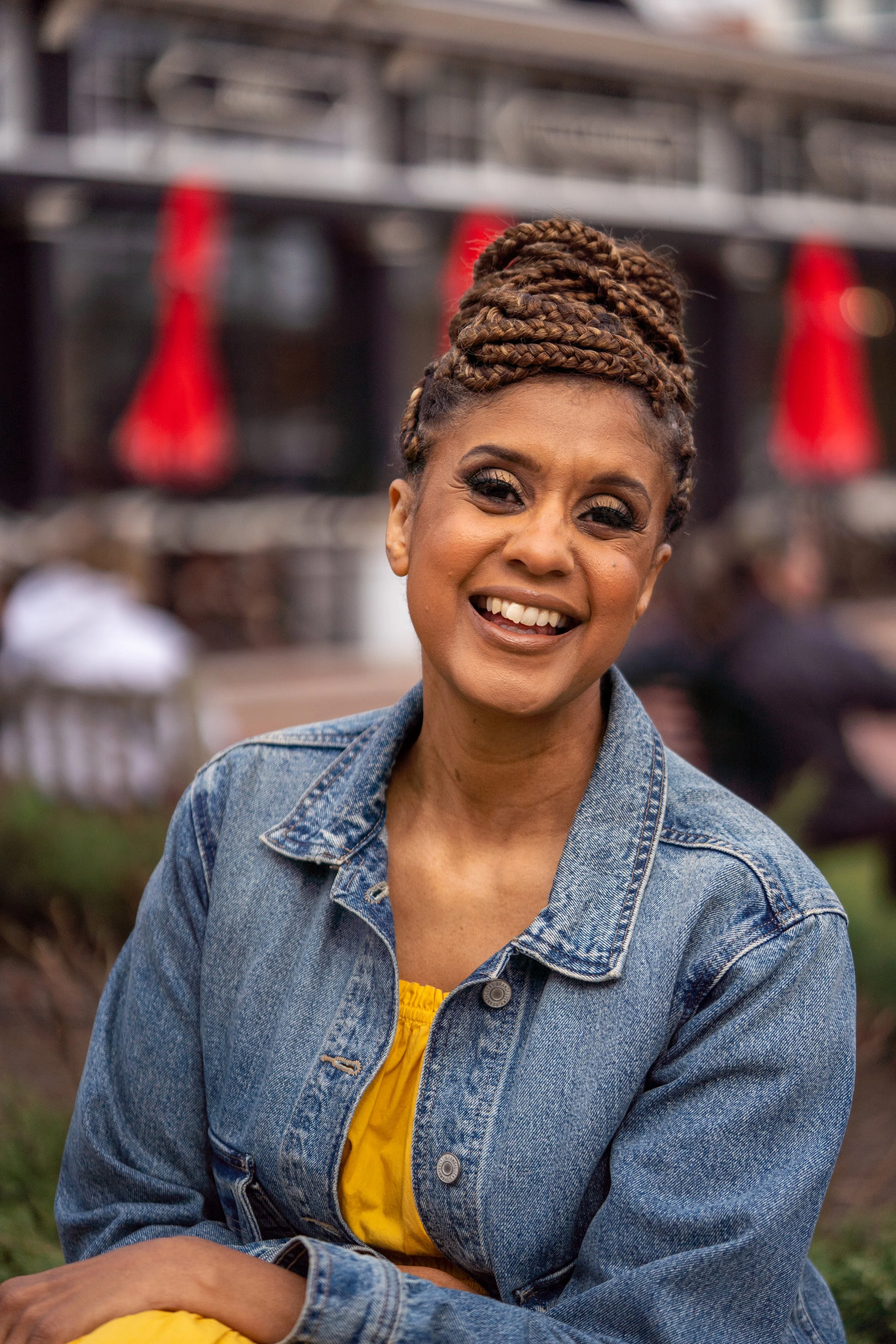 Evelyn Fordham Goodman with braided hair, smiling outdoors, wearing a denim jacket over a yellow top.