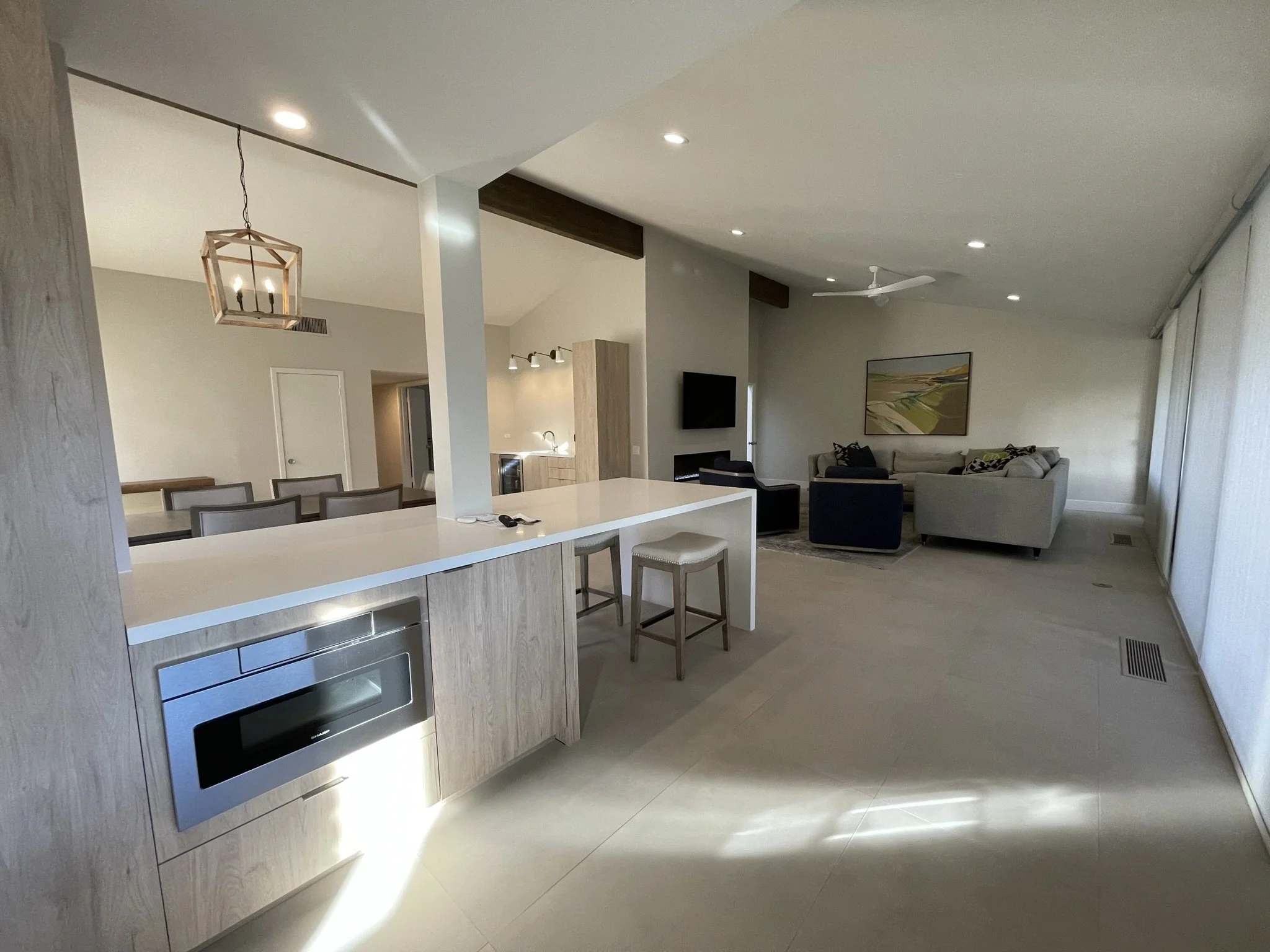 Open-concept living space with a kitchen, dining area, and living room, featuring modern decor, a hanging light fixture, a ceiling fan, and a large painting on the wall.