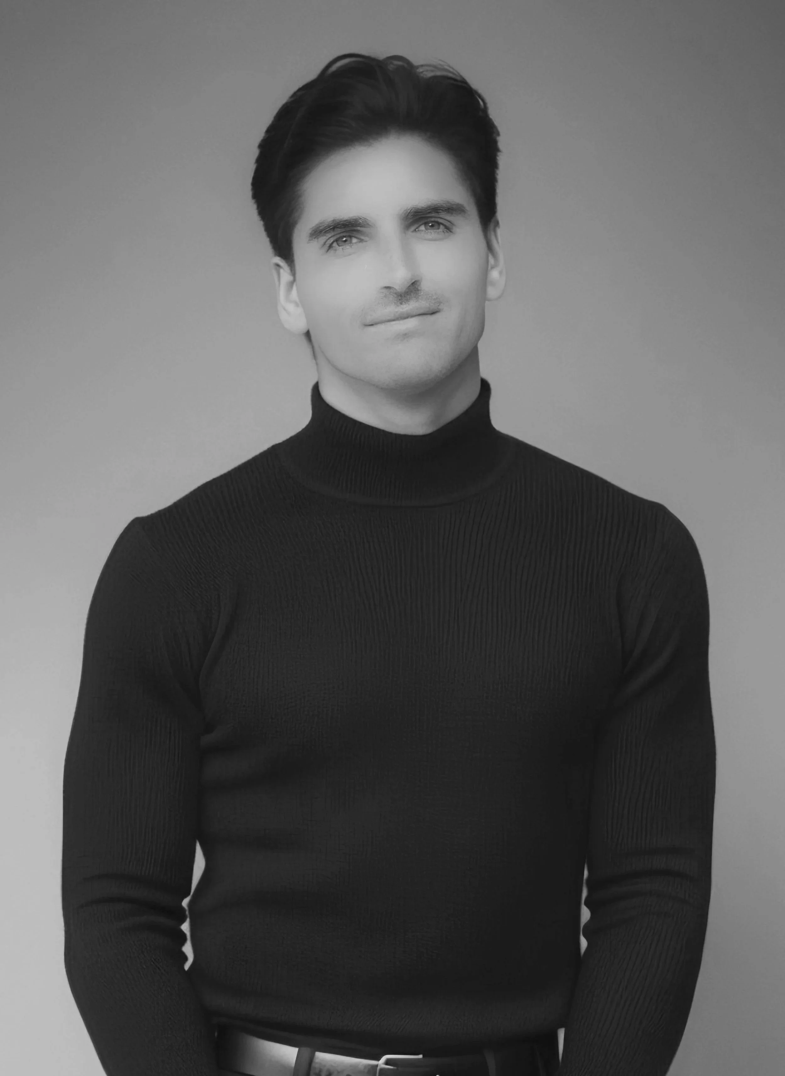 Black and white portrait of a young man with dark, styled hair, wearing a black turtleneck sweater, looking slightly to the camera's right with a subtle smile.