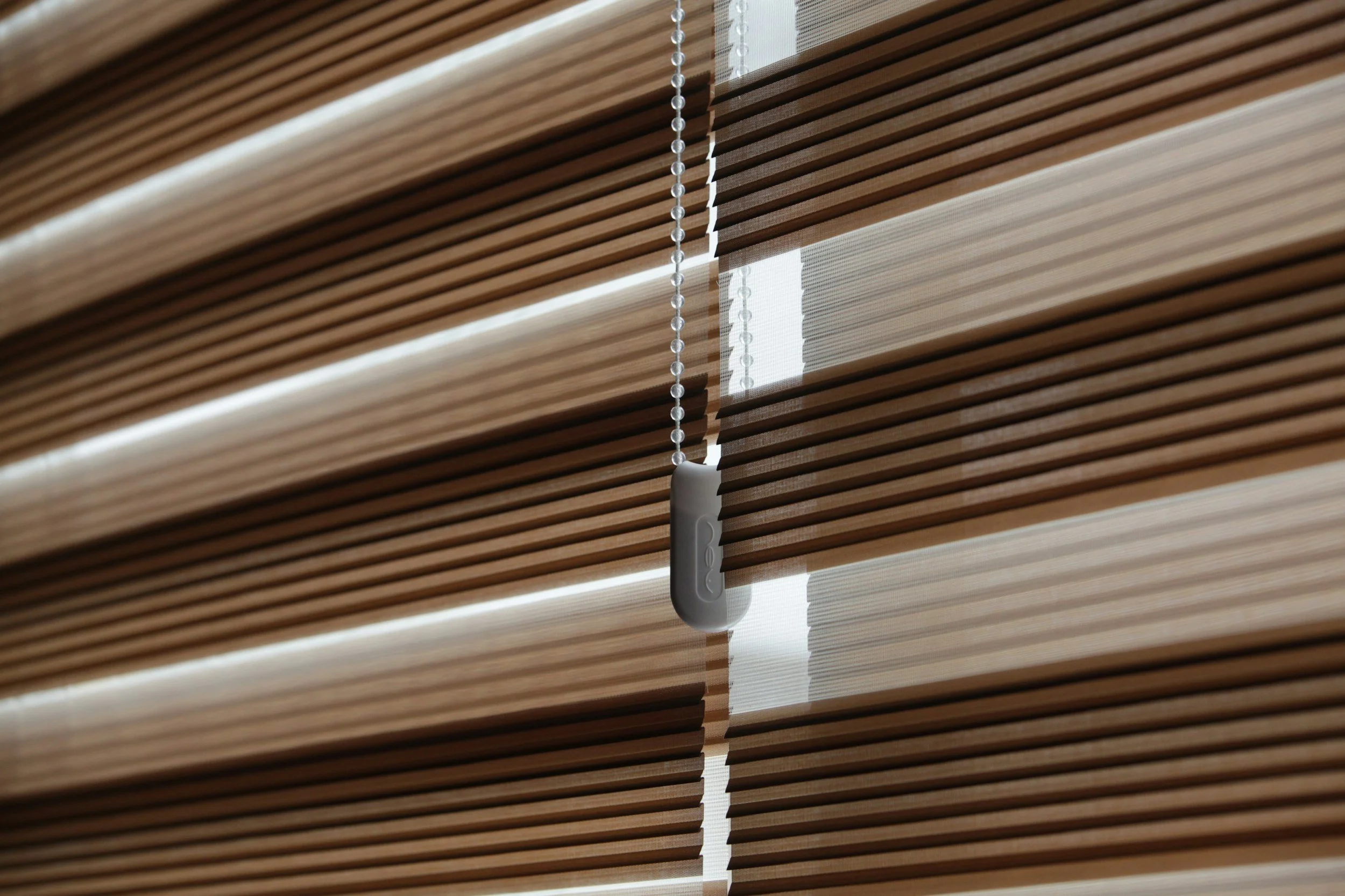 Brown window blinds with a hanging chain and a white control device.