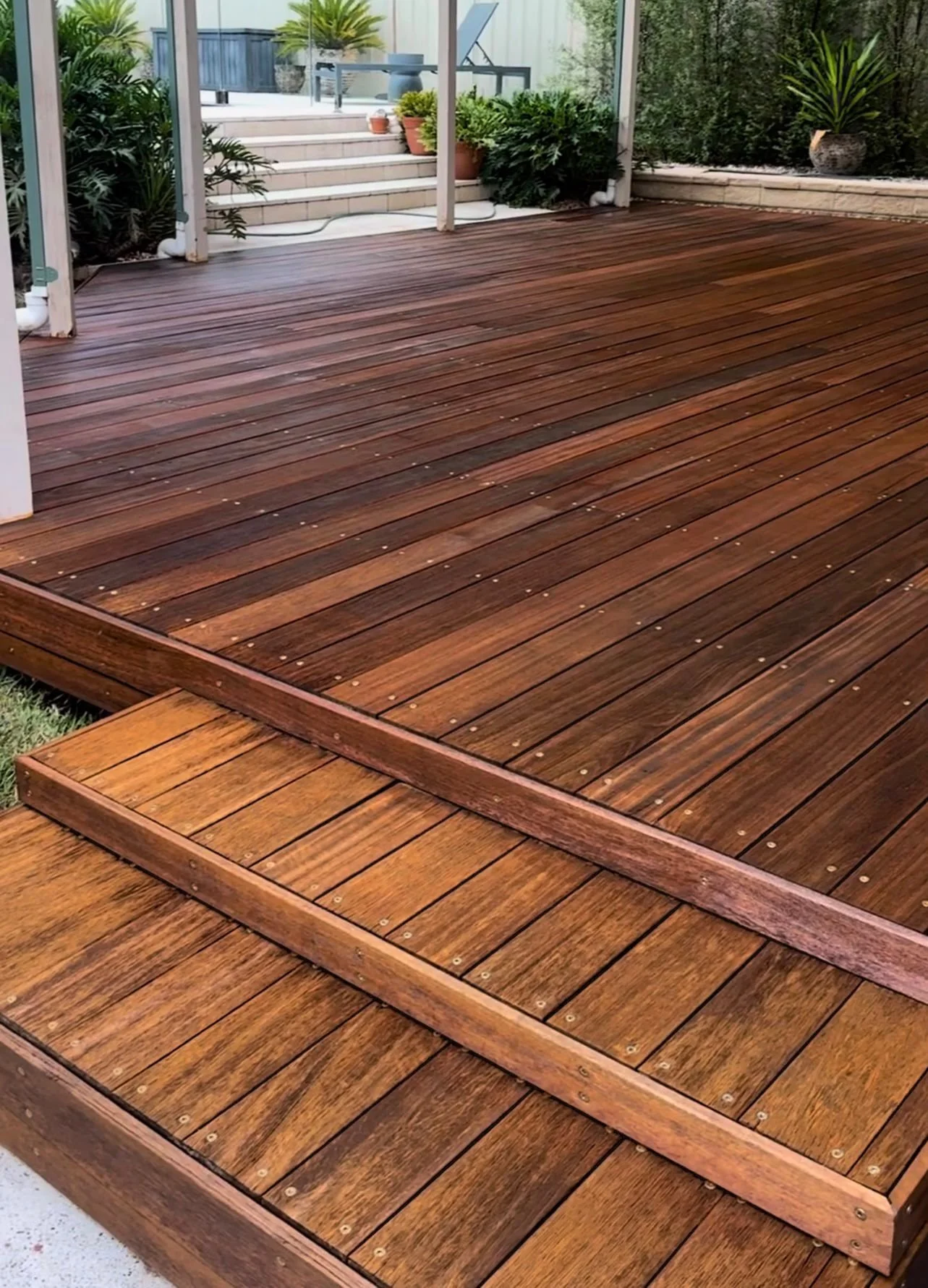 A wooden deck with multiple steps, surrounded by plants and patio furniture.