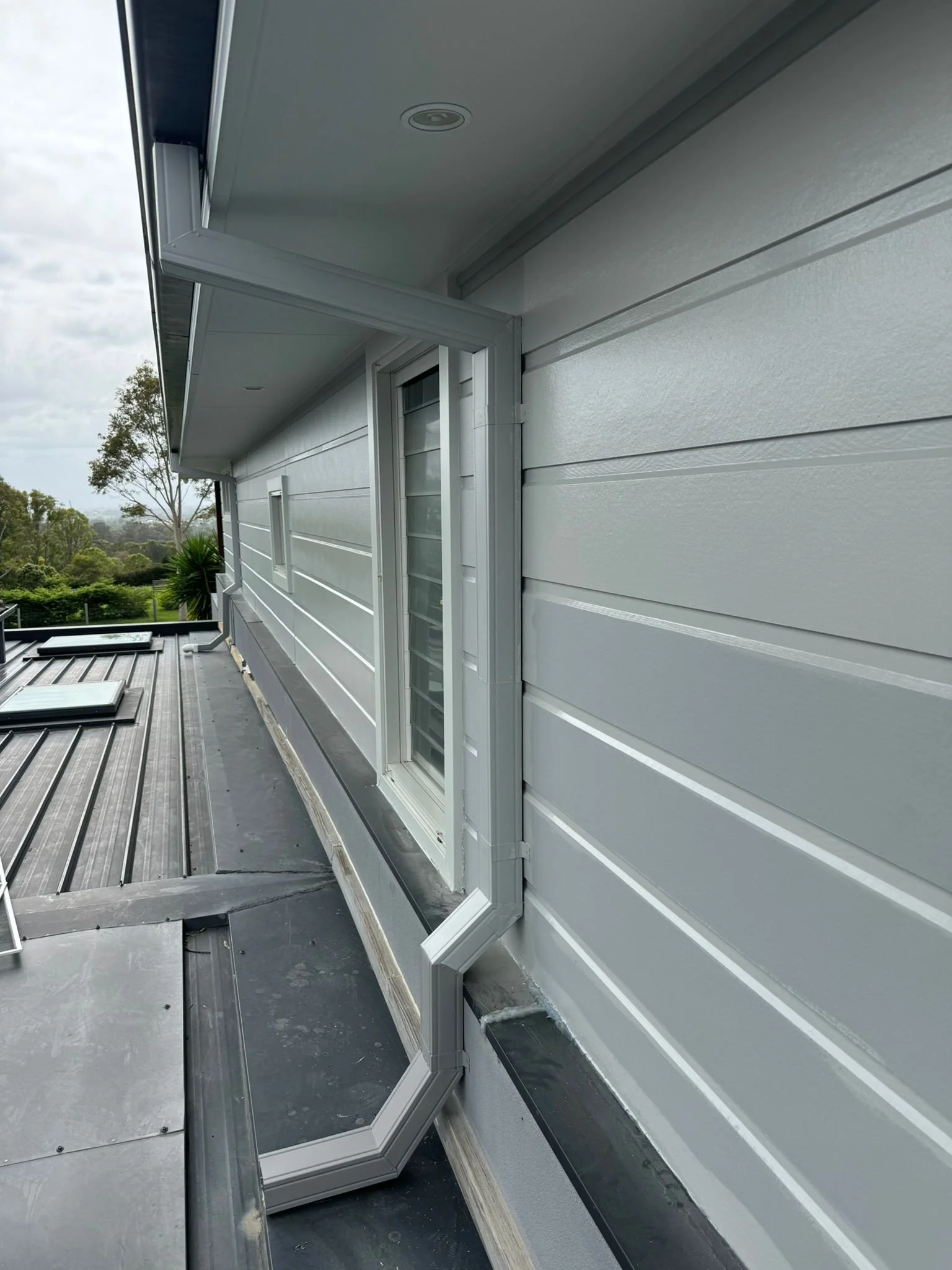 Exterior view of a light gray house with horizontal siding, showing a window with an open window awning and a rooftop with solar panels.