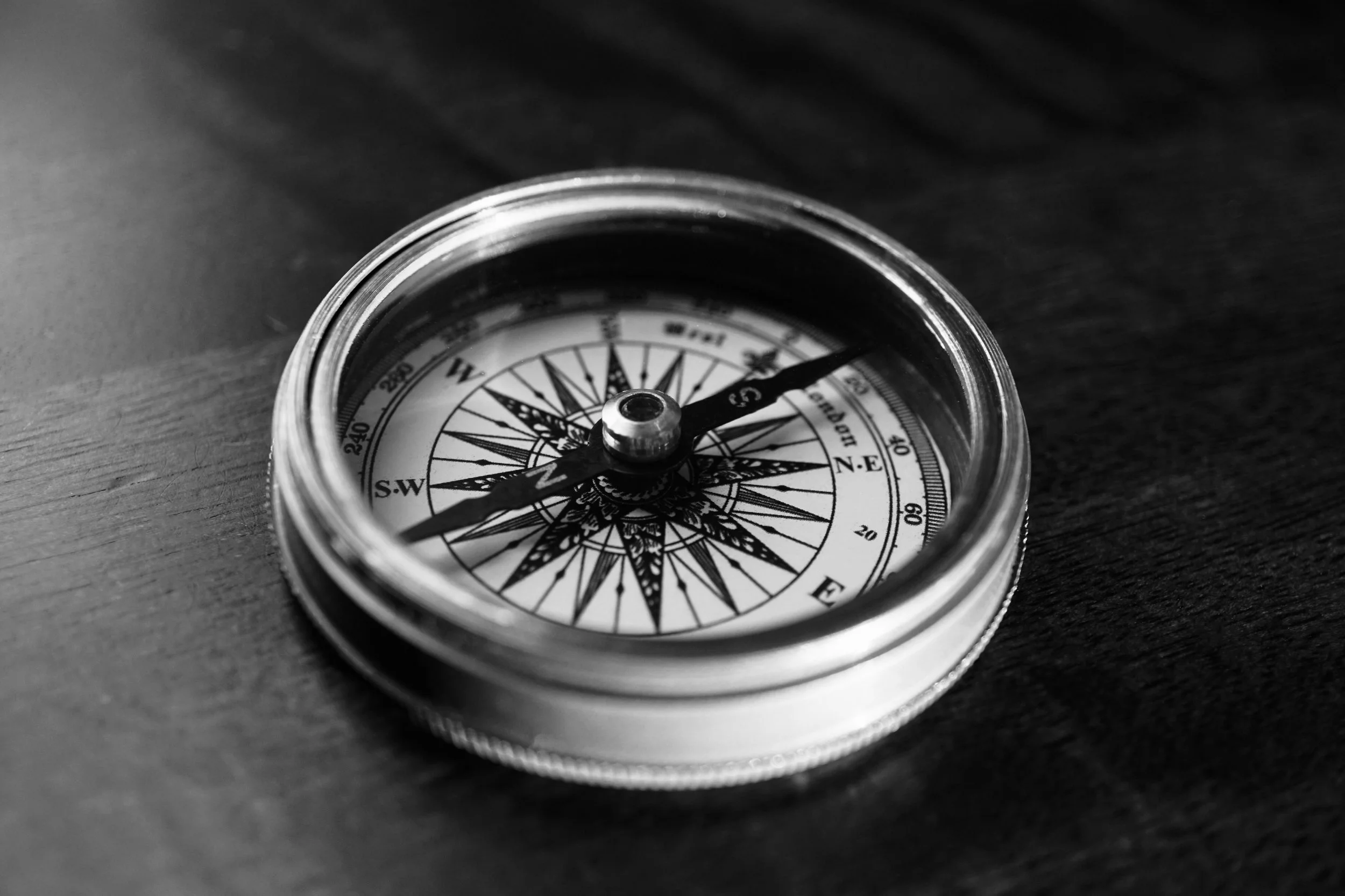 Black and white photo of a compass with a glass top, resting on a dark wooden surface.