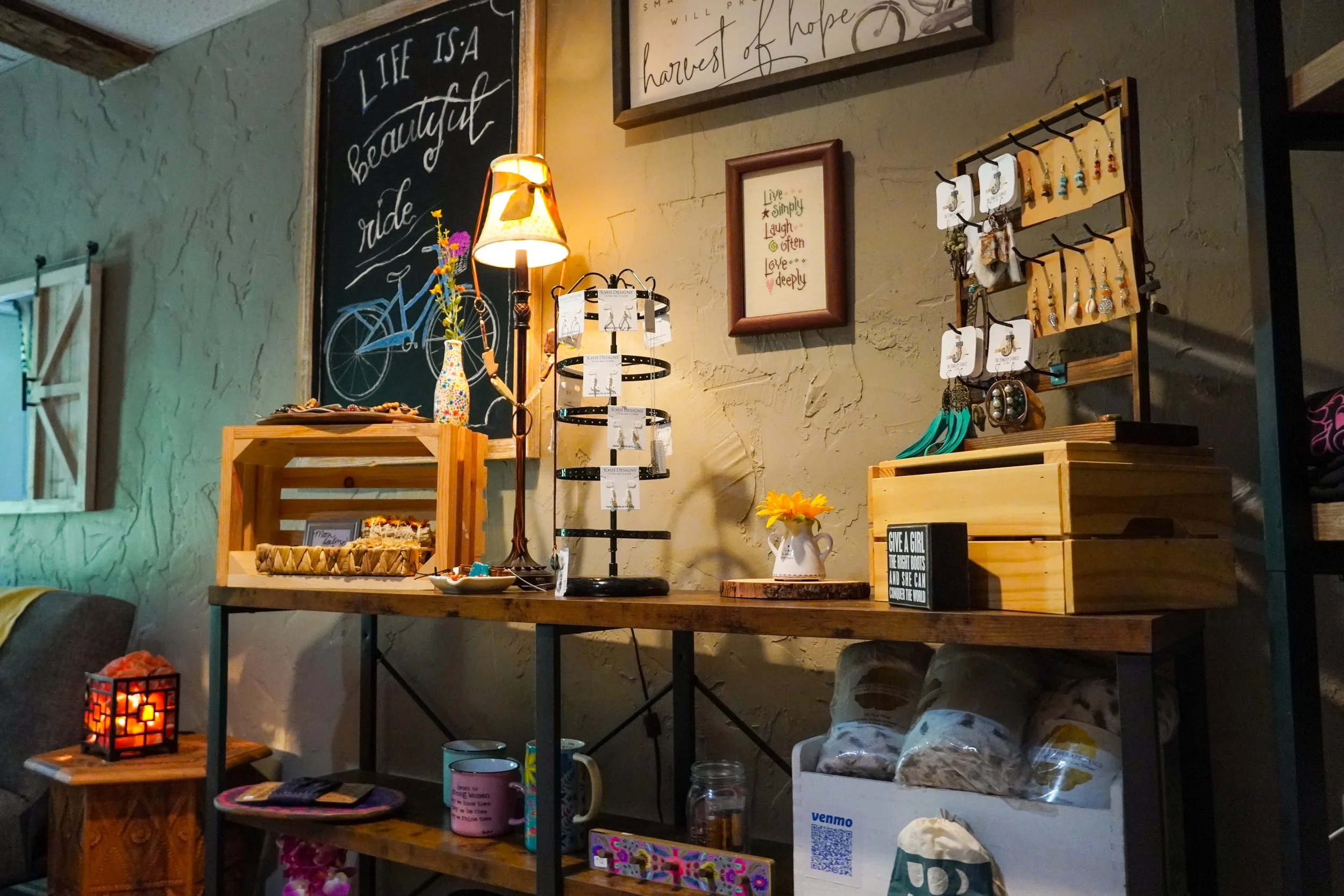 A display shelf arrangement with decorative items, small jewelry stand, framed quotes, and a chalkboard sign that reads 'Life is a beautiful ride' in a cozy, rustic interior.