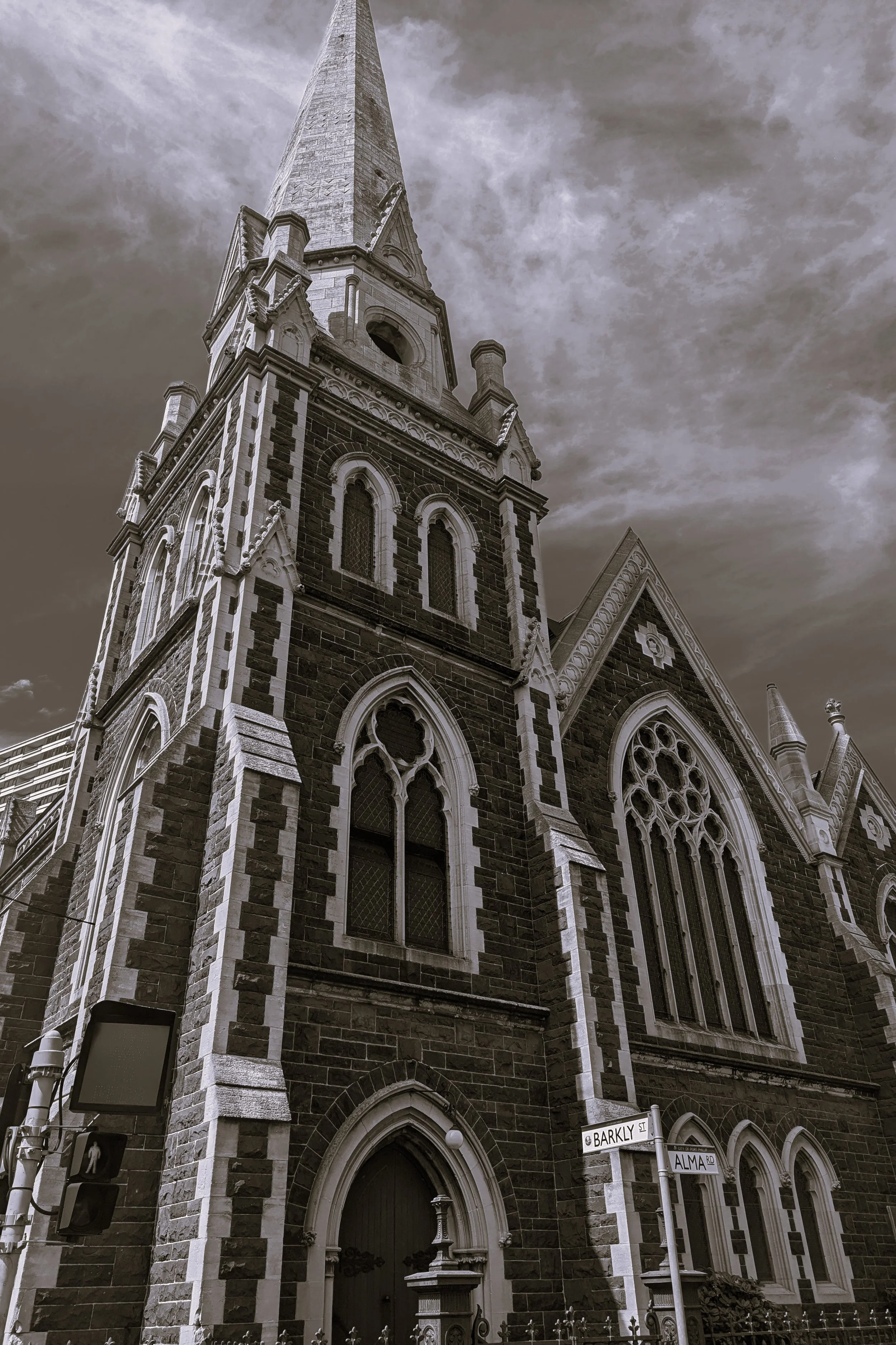 A tall, Gothic-style church with a spire, ornate stonework, arched windows, and a darkened entryway, situated on a street corner in an urban area.