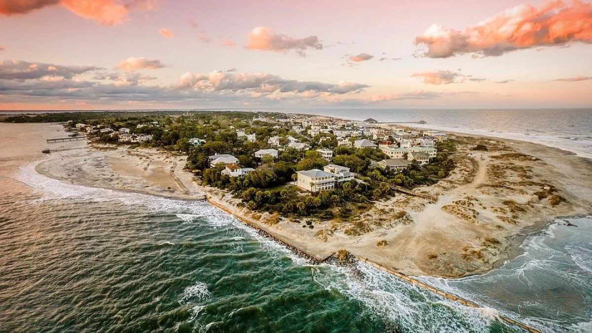 Aerial view of a coastal town with houses along the shoreline during sunset, with the ocean to the left and sandy beaches to the right.