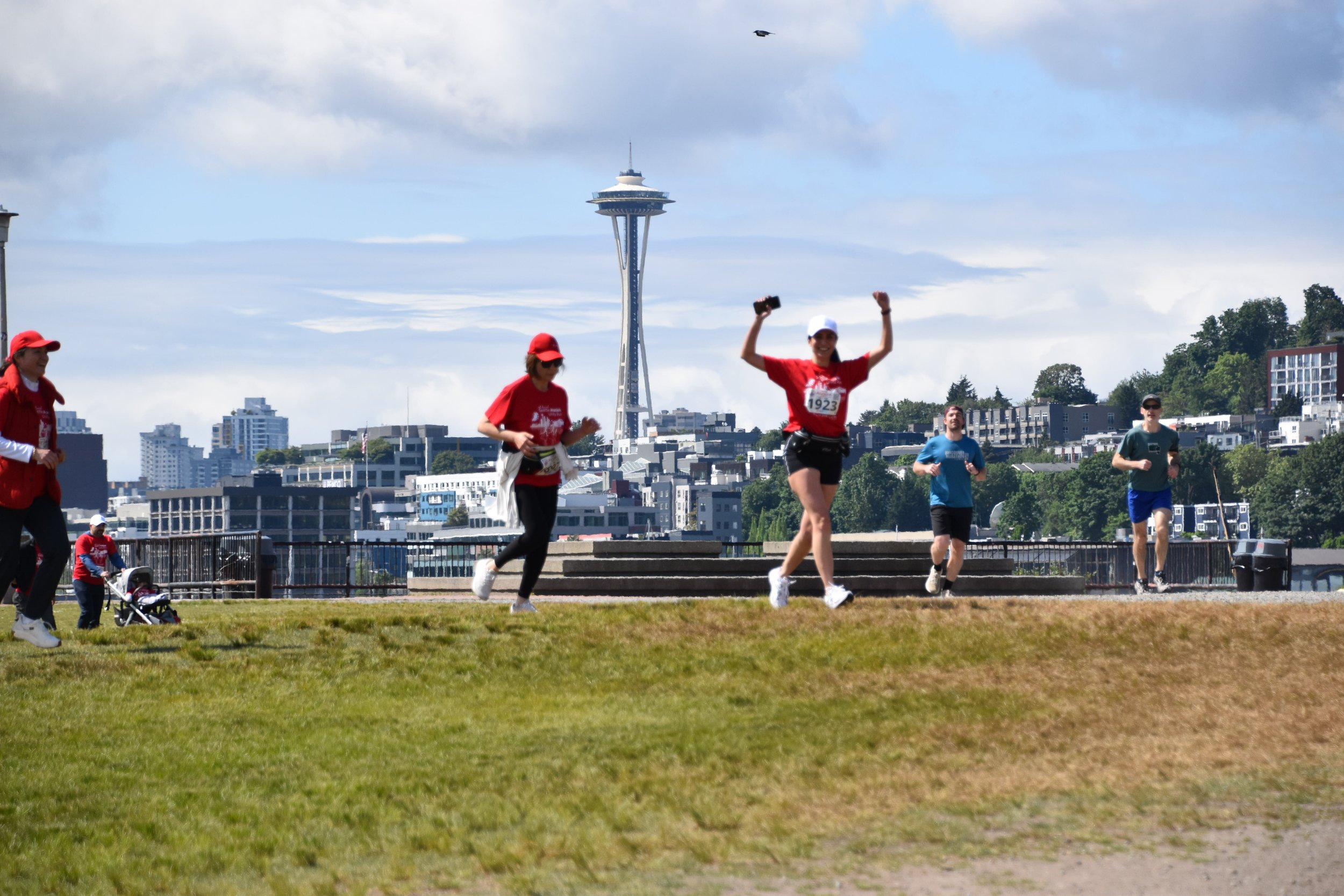 People participating in a winter race run through snowy terrain with an archway overhead and orange cones, while others watch and walk nearby.