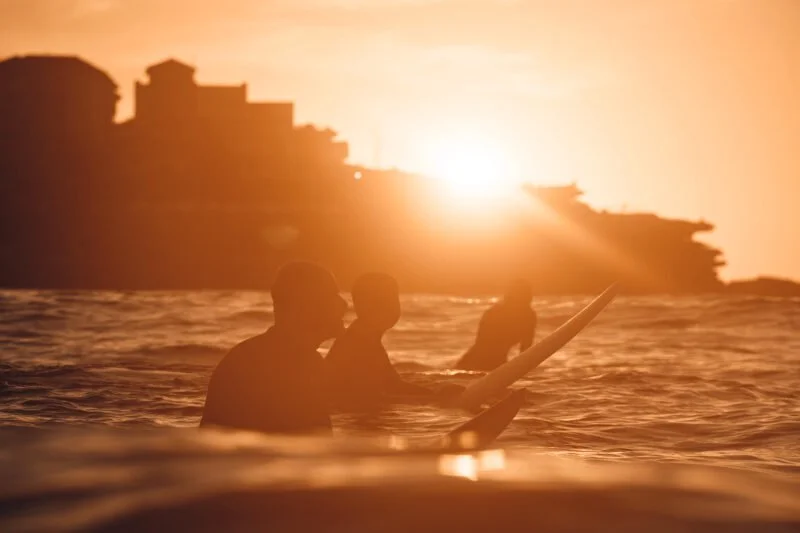 Silhouettes of three people surfing in the ocean at sunset