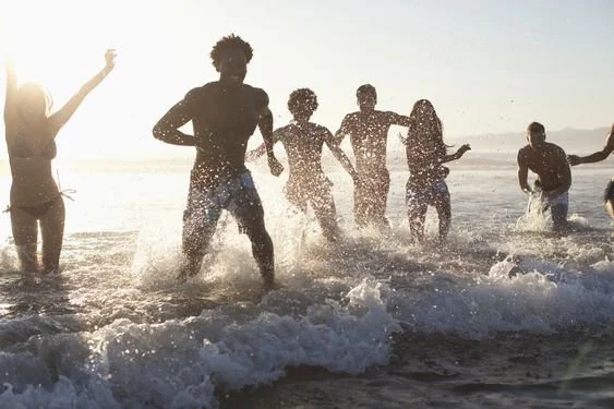 Group of people playing and running in the ocean waves at the beach during sunset or sunrise.