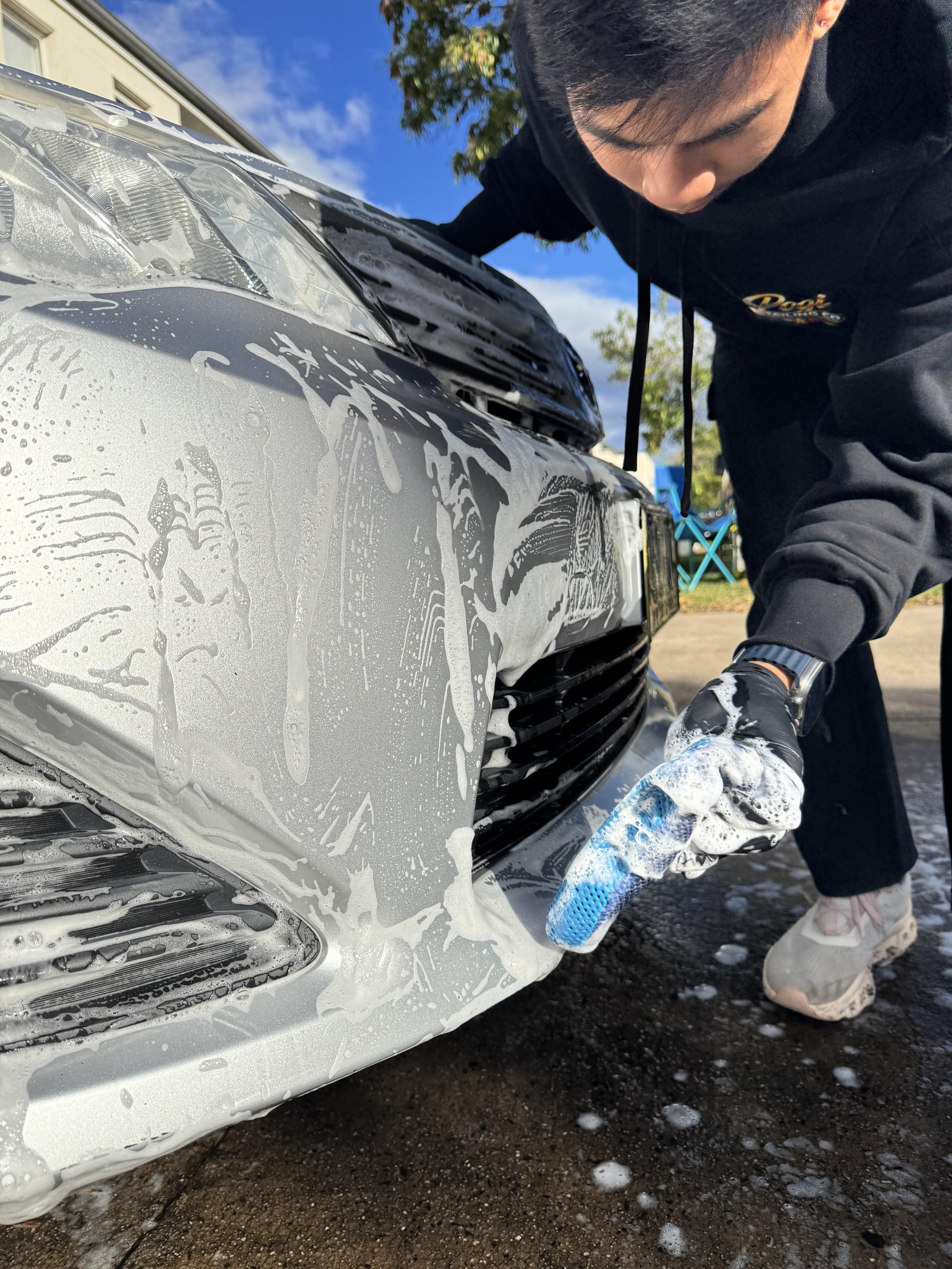 Professional mobile car detailing service cleaning and restoring the exterior front bumper of a vehicle, removing dirt and grime for a clean, glossy finish.