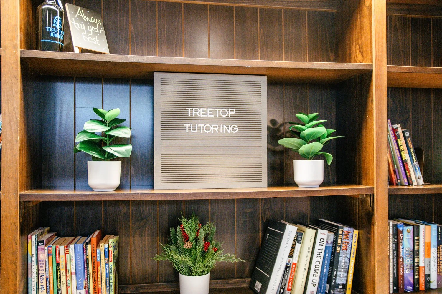 Bookshelf with books, potted plants, and a sign that says 'Always try your best' at the top; Center sign reads 'Tree Top Tutoring.'