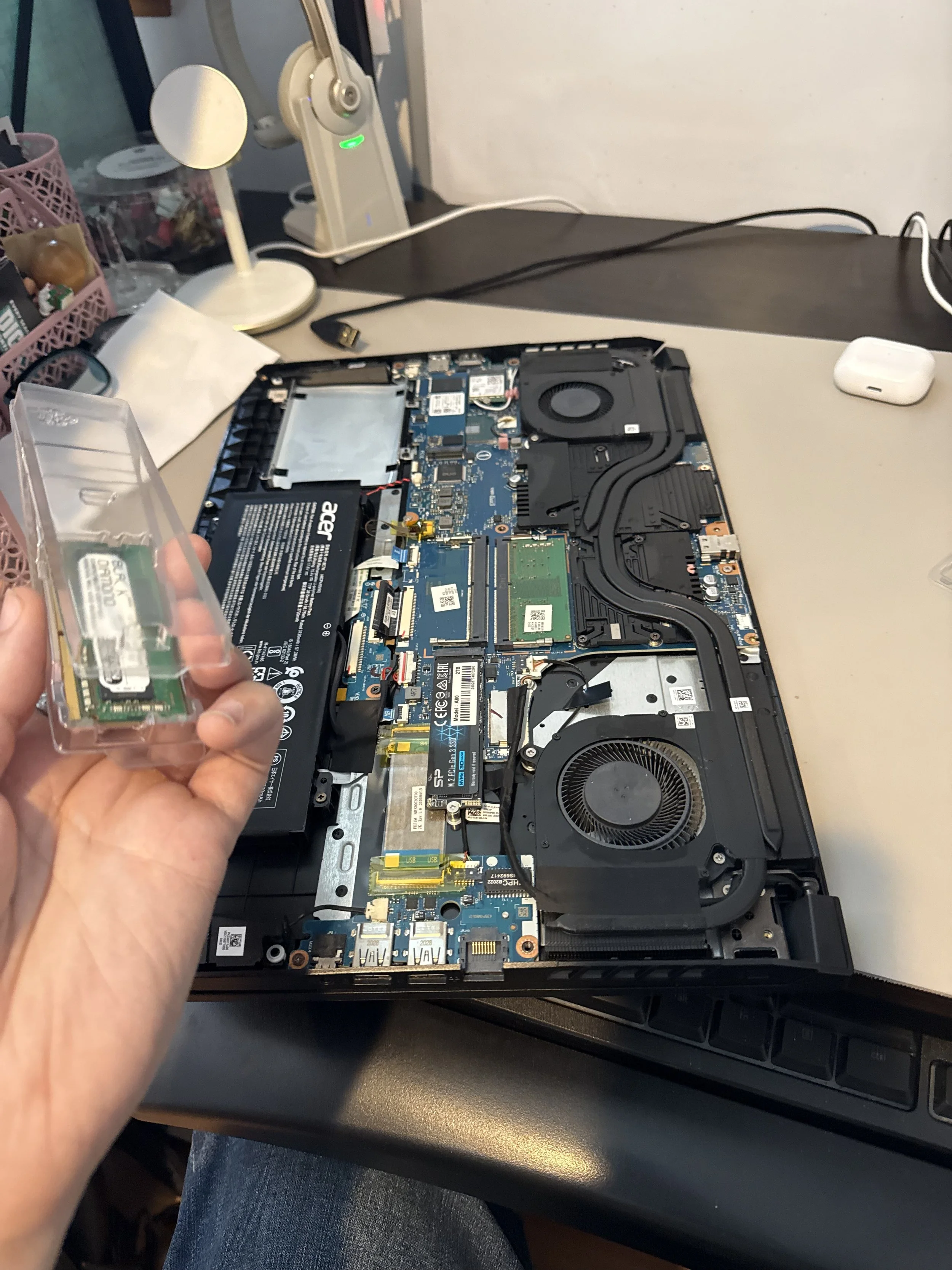 A person holding a small computer component over an open laptop with its internal hardware visible on a desk.