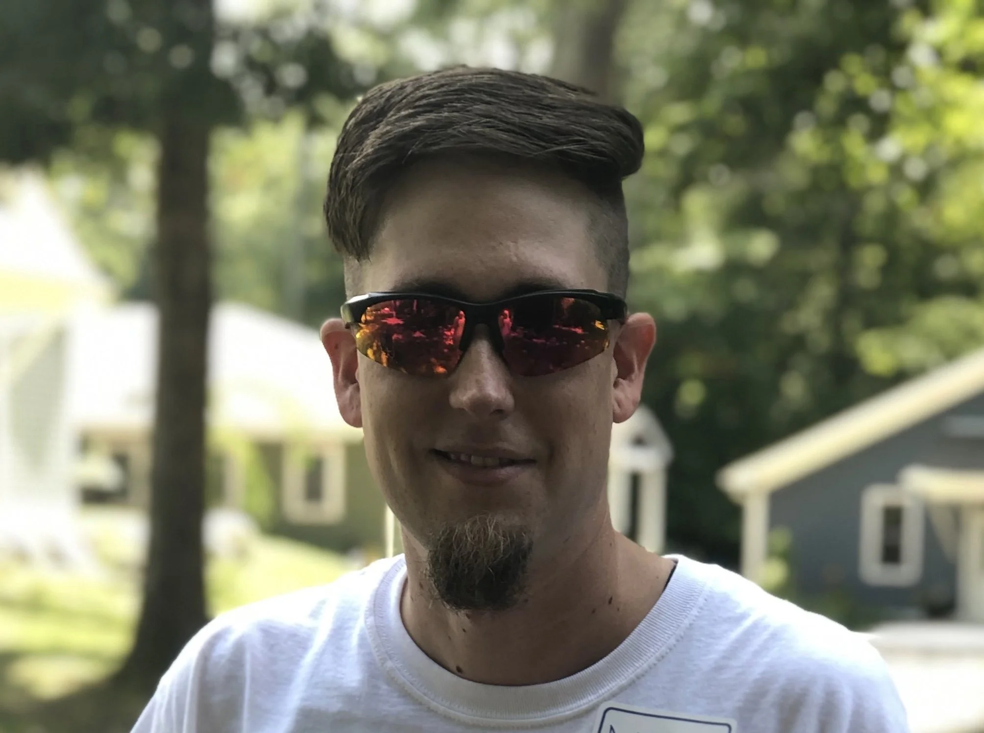 A man wearing sunglasses outdoors, smiling.
