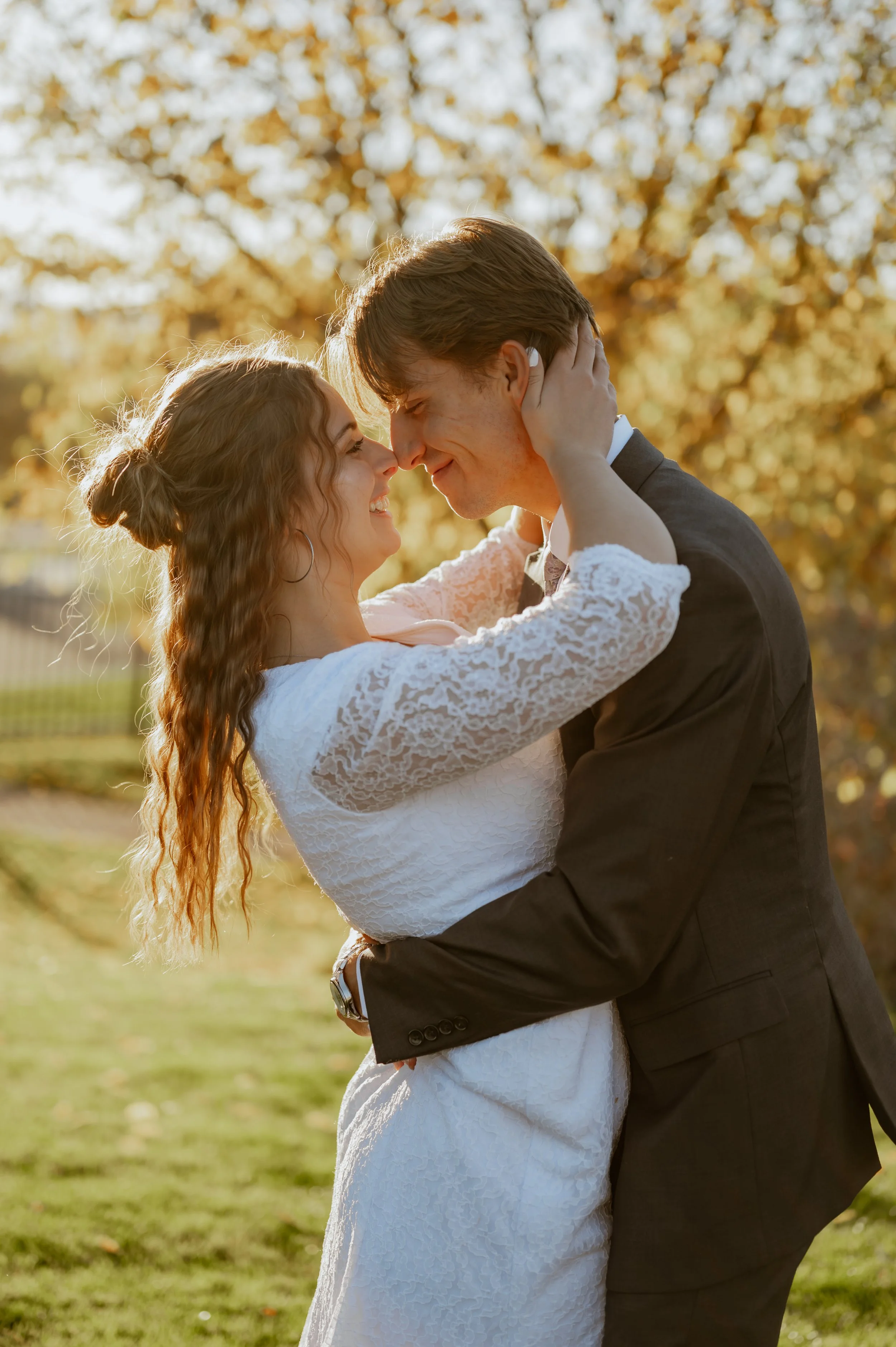 A couple dancing outdoors in the fall, smiling and touching foreheads, with trees with golden leaves in the background.