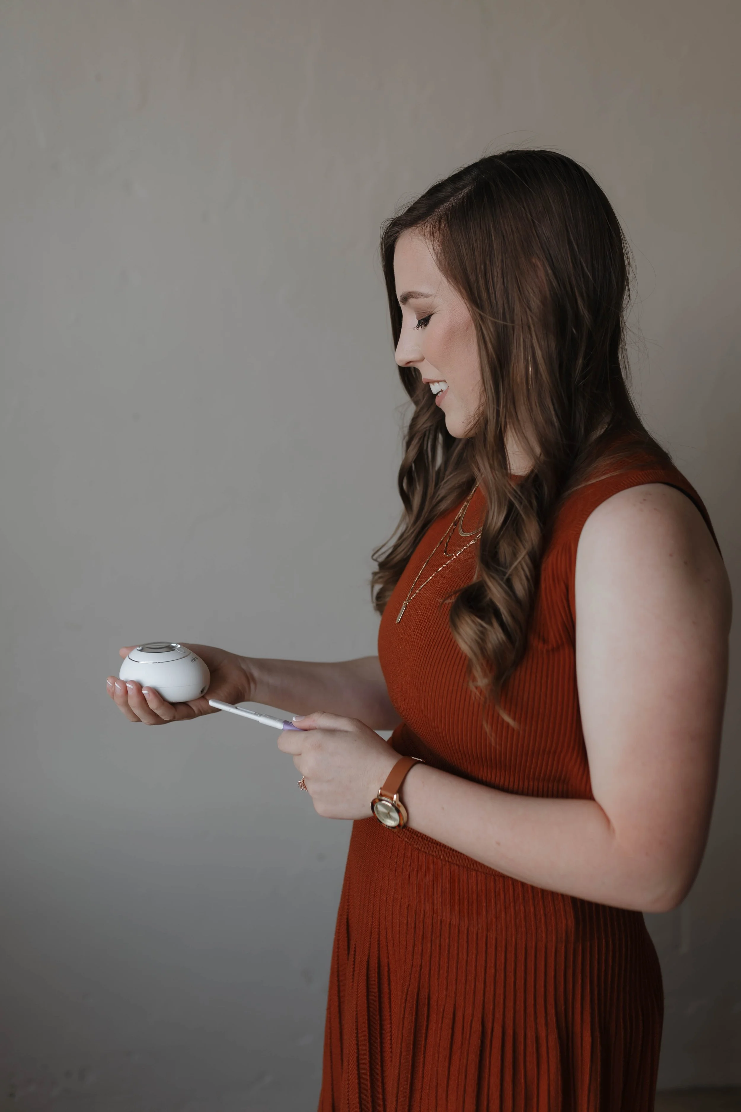 A woman in a sleeveless brown dress holding a blood glucose monitor and testing her blood sugar levels.