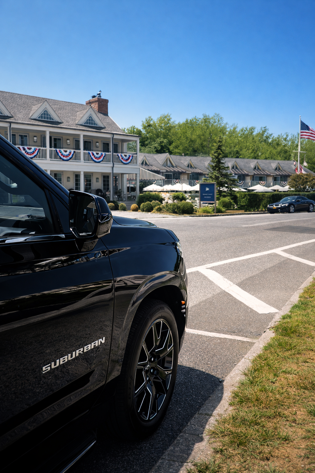 Close-up of a black car parked on the street in front of a building decorated with American flag bunting and patriotic decor, with a clear blue sky and trees in the background.